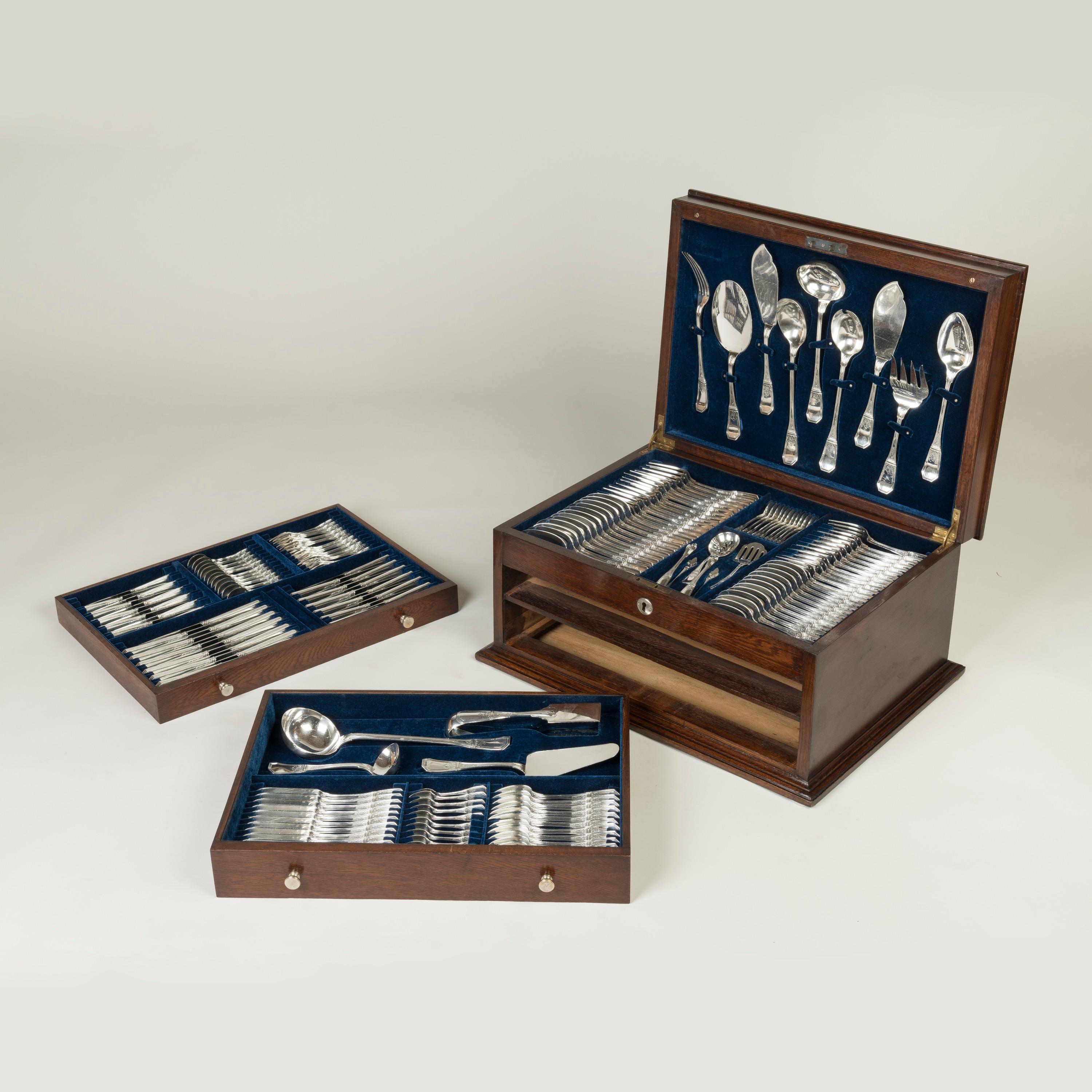 Este extenso juego de 13 cubiertos para 12 personas de estilo Regencia, con detalles neoclásicos en las asas, en su carácter y estado originales, sin monograma, y guardado en su caja ajustada y forrada. Todas las piezas son de plata 950, están