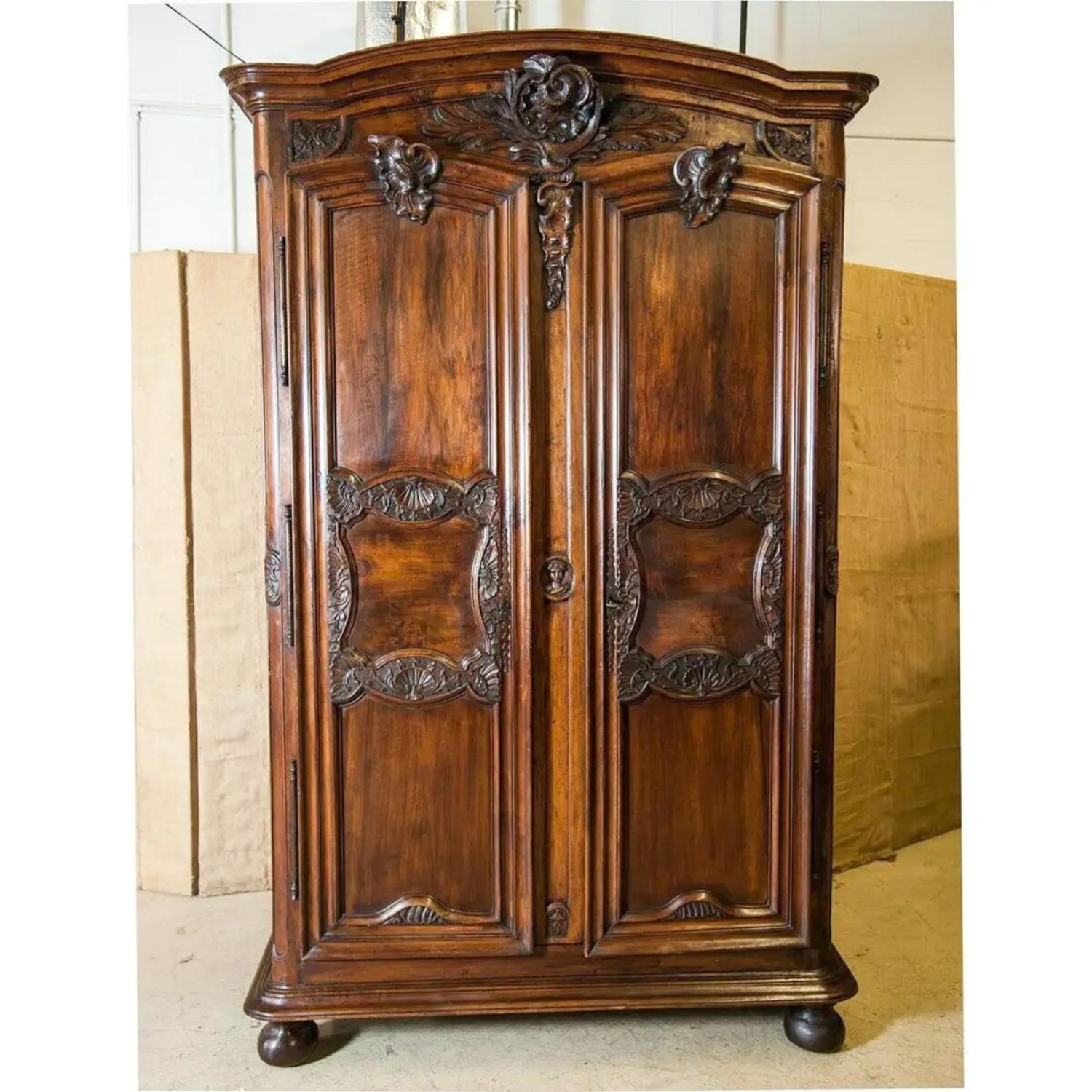 A monumental 18th century French Régence period chateau armoire handcrafted of solid walnut by talented artisans in Lyon, circa 1720, having a chapeau de gendarme crown atop an intricately hand carved frieze adorned with beautifully carved rocaille