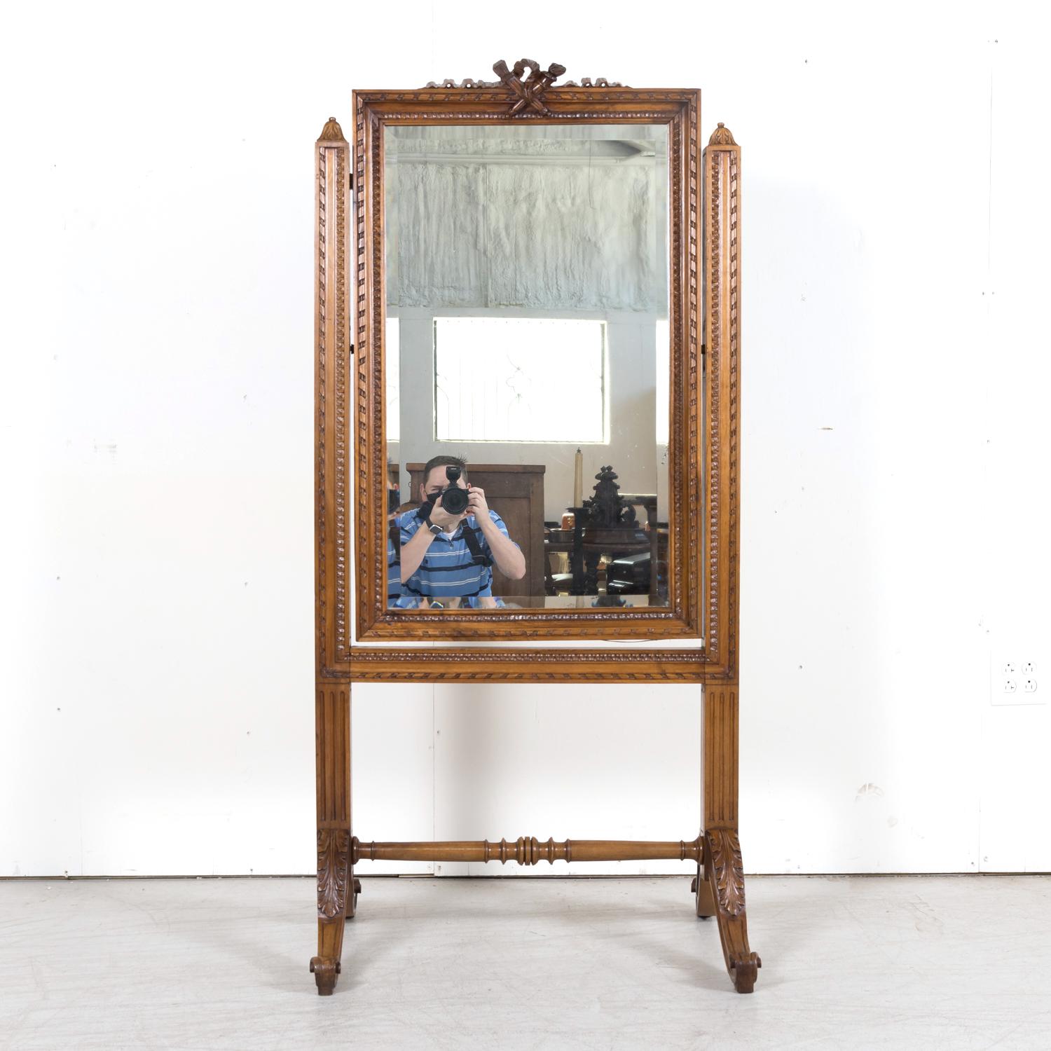A exceptional 19th century Louis XVI style cheval dressing mirror handcrafted of walnut, circa 1880s, having the original beveled mirror inside a beautifully carved walnut frame featuring typical neoclassical motifs from the period. The carved crest