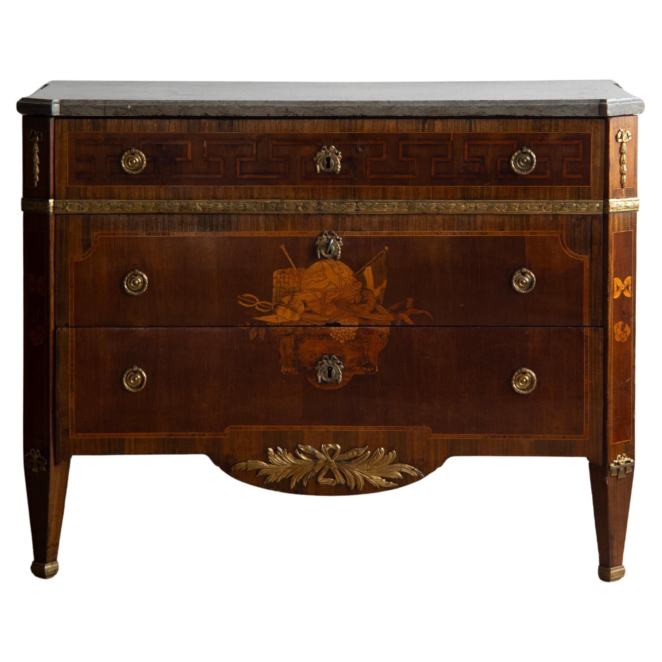 Exceptionnelle commode gustavienne du début du XIXe siècle plaquée d'amarante, de bouleau, de jacaranda et d'érable. Dessus en pierre calcaire, ferrures en laiton doré, boîtier et côtés à la grecque, façade avec marqueterie symbolisant la navigation