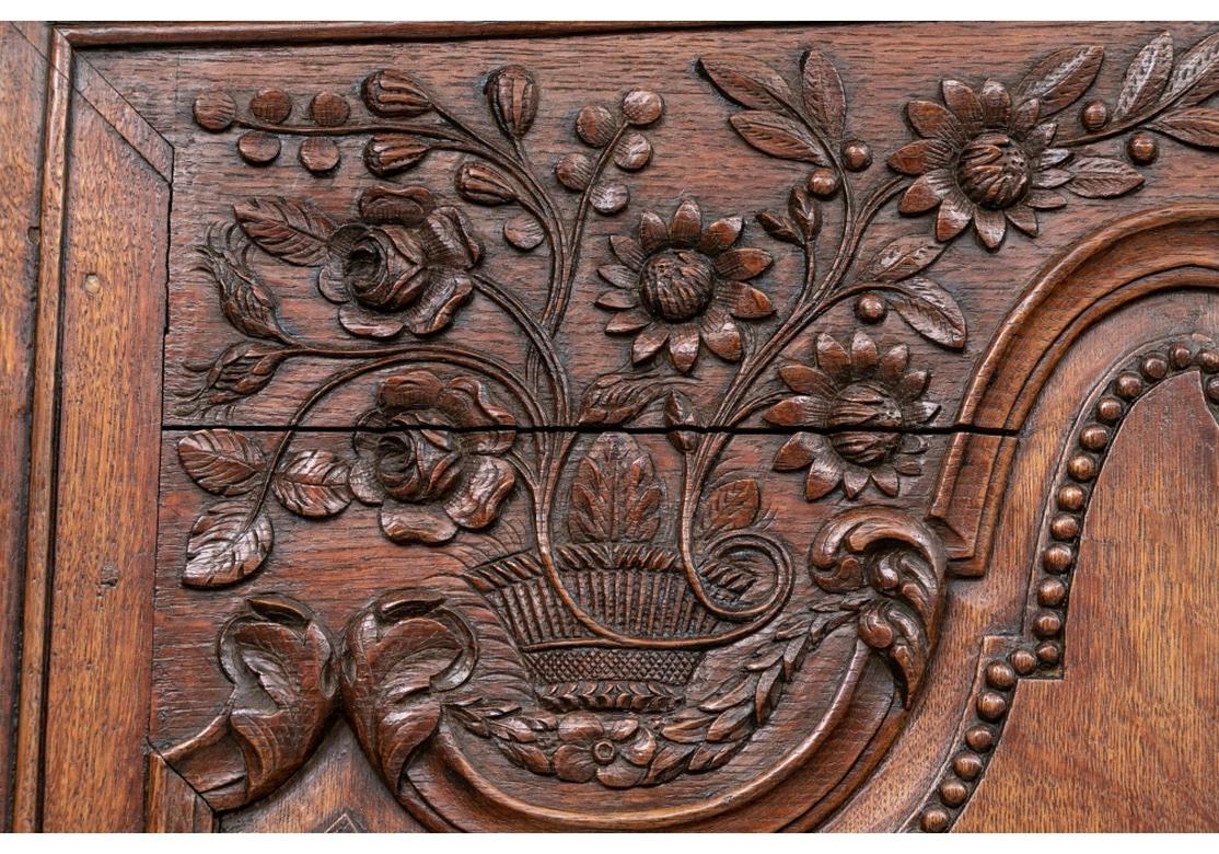 Grand 19th century French armoire, the crown heavily carved with intricate and dimensional flowers and leaf basket, flanked by corner floral motifs. The armoire with two doors having full length covered brass hinges, raised panels trimmed with