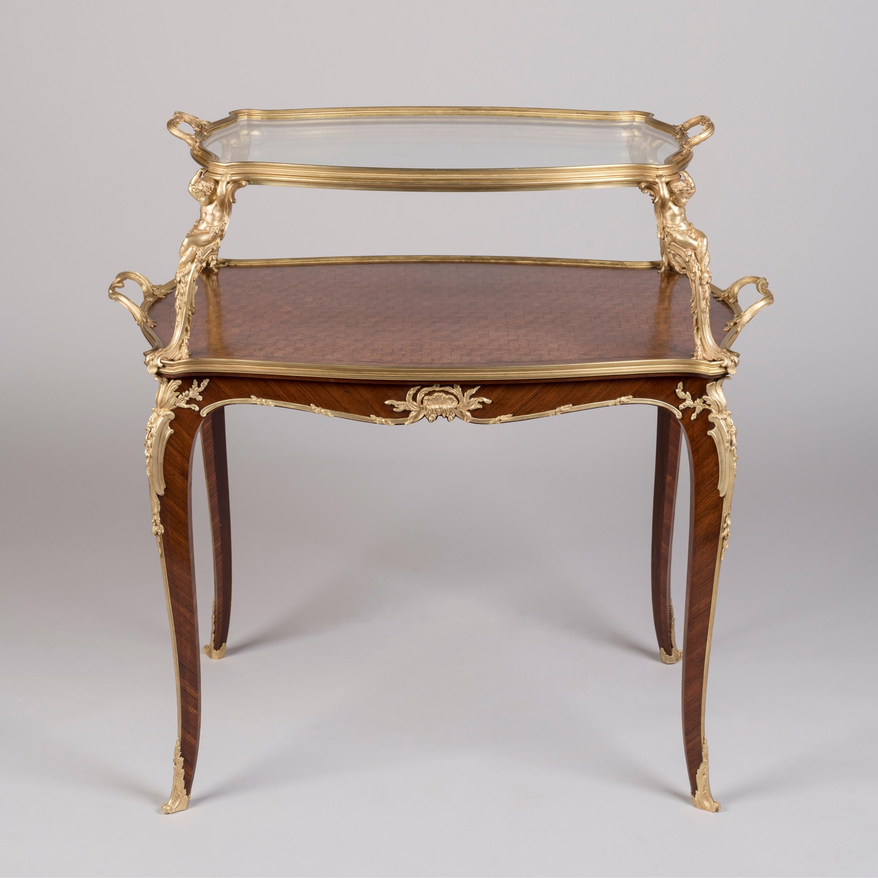 A Very Fine Louis XV Style 
Two-Tier Table à Thé

By François Linke. Index no. 610

The serpentine dual-handled upper-tier with removable glazed tray supported by four gilt bronze putti tritons, the kingwood lower-tier inlaid with cube satiné