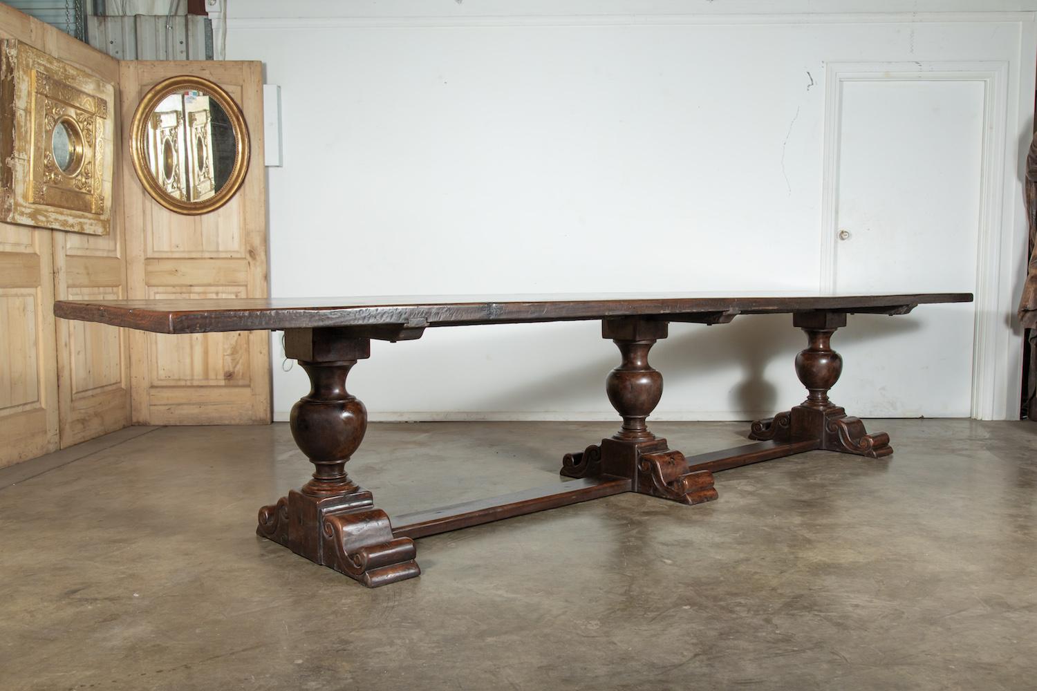 A monumental 19th century Louis XIII style French chateau trestle table, having a thick two plank solid walnut rectangular top, it exudes a rustic elegance. Supported on a walnut base with three hand carved pedestal legs, each resting on a carved
