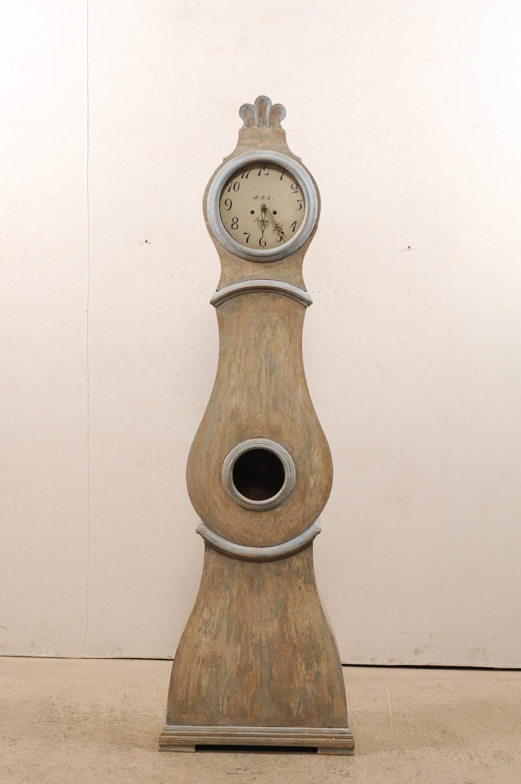 A beautiful Swedish painted wood Mora clock from the 19th century. This antique Mora clock from Sweden features a fanned carved wood crest adorning it's head, a teardrop-shaped door and belly, and a flat base which is slightly lifted upon