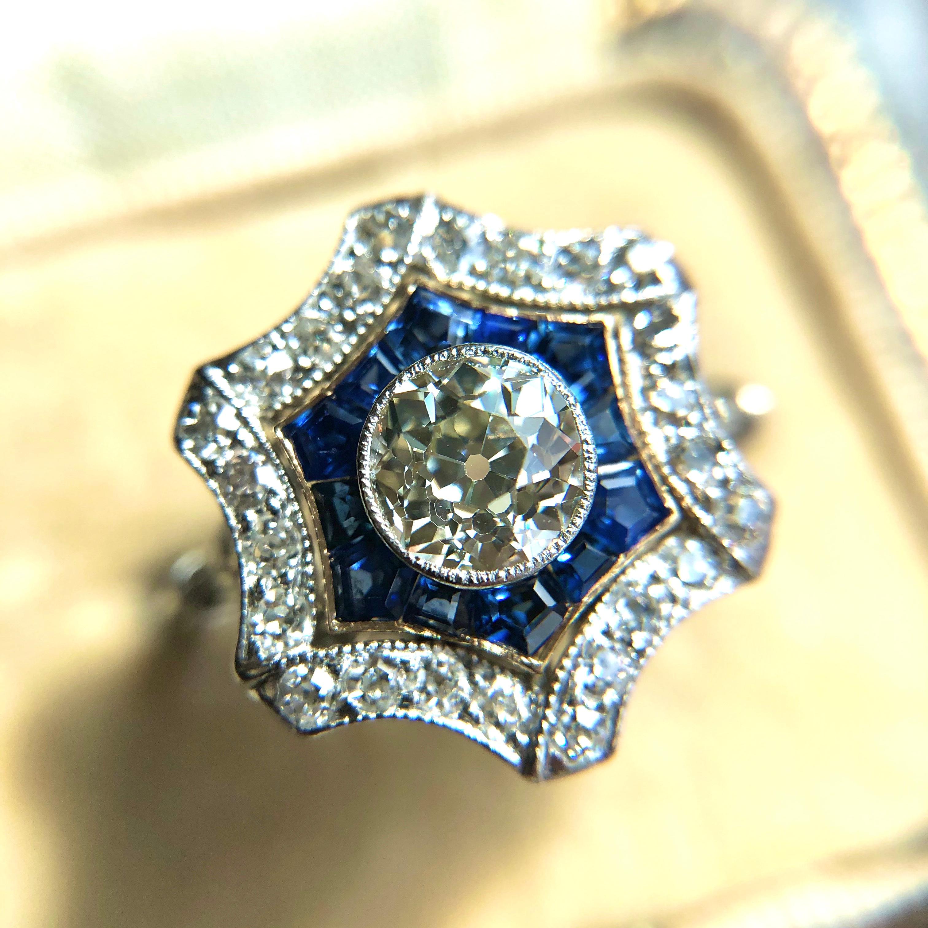 Sapphire and diamond ring. This charming ring, designed as a hexagonal rosette, is deceptively simple. With an outer border designed as a folding ribbon, the openwork centre appears to float within it: a contrasting border of yellow gold encloses