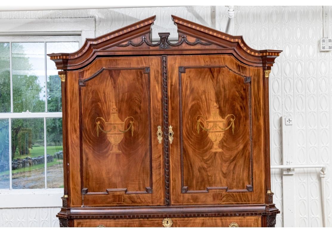 A monumental Dutch Inlaid Cabinet likely dating to the 18th Century. Raised on four legs with three long drawers all with intricately designed brass hardware. Above are a broken Arch pediment top with dark wood carved swags and a delightful