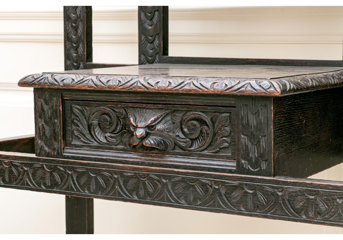 A fine Hall Stand with overall hand carved frame with Bobbin style supports with cap finials, central beveled mirror with shelf,  ten coat/ hat pegs, and a single drawer with a handle of a carved and snarling animal head. The stand is stained in a