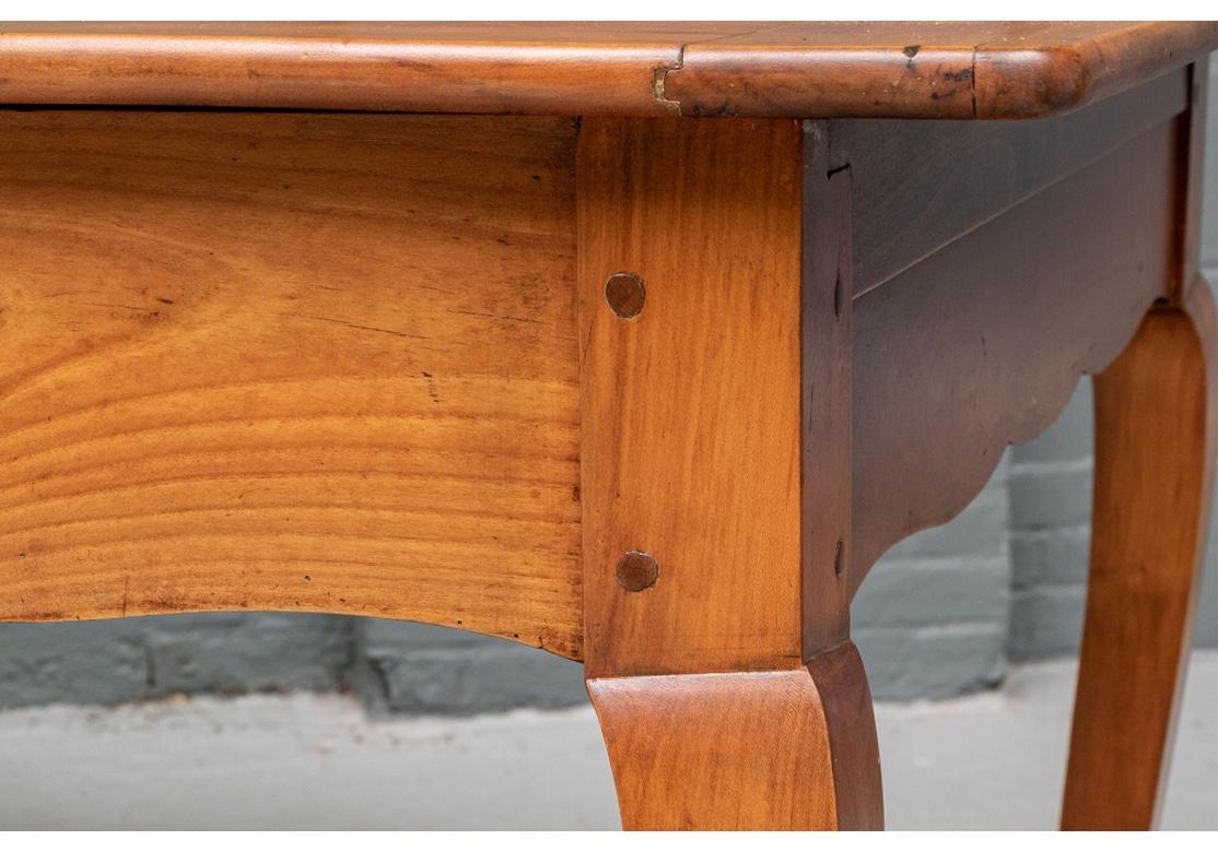 An uncommonly fine traditional antique cherry French farm table with bread board top, two opposing drawers, scalloped apron, exposed peg construction and resting on cabriole legs.
Dimensions: 36