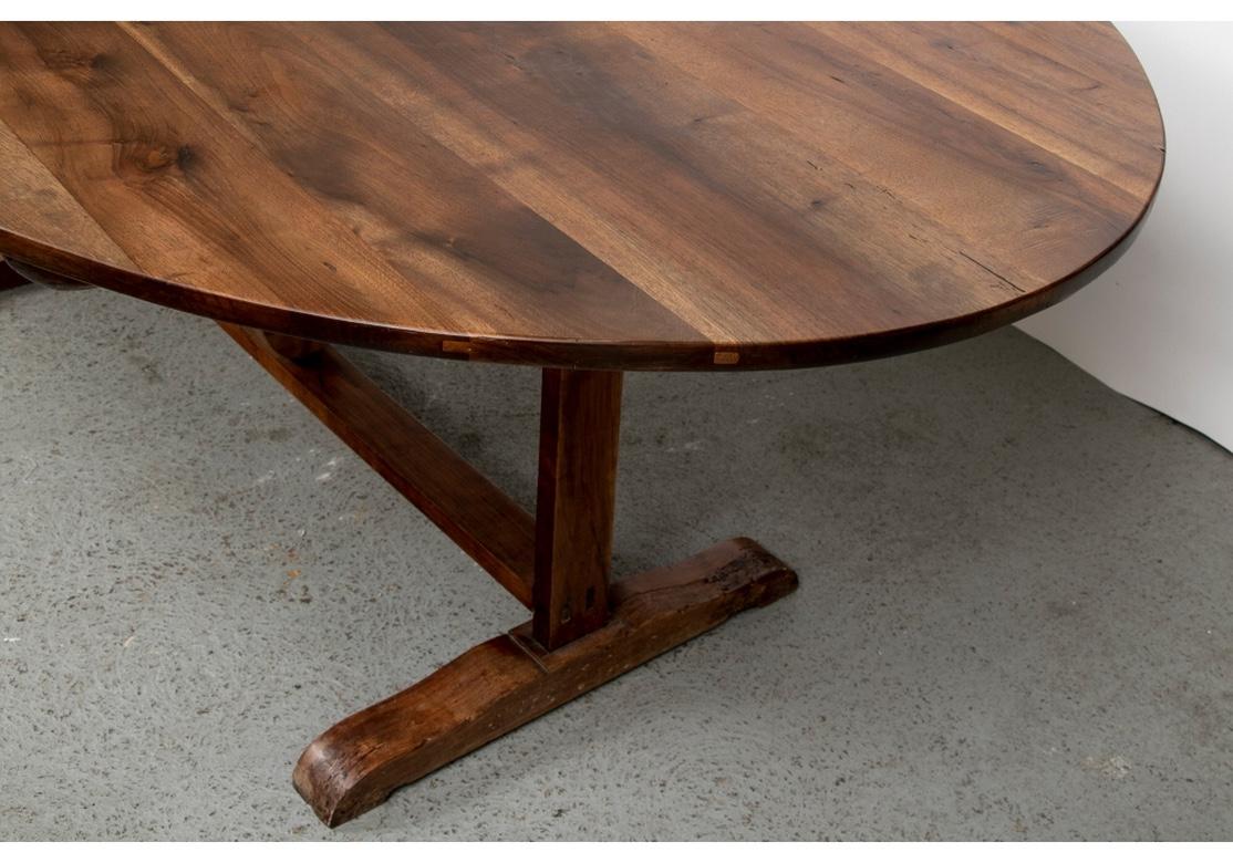 An oval folding vendage table with a burled plank constructed top. The base with two end supports on extended sledge feet. The center with a collapsible shaped and curved support with a stretcher. Tables of this kind were in regular use in the