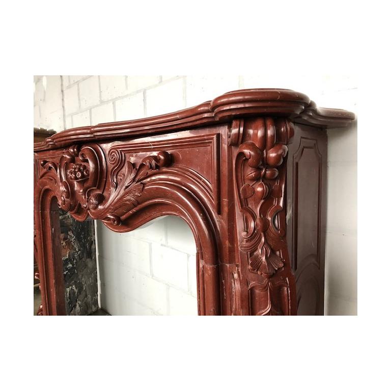 This beautiful, antique Louis XV fireplace was made out of the highly-valued red Griotte marble, during the 18th century.
Extremely curved and decorated with flushy sculptures. The center of the frieze is ornated with a vase and fruit.
The winding
