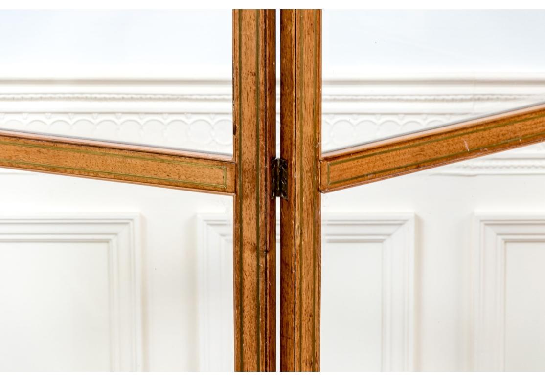 Un divisorio antico finemente lavorato ed elegante. L'antico paravento a tre pannelli è costruito con pannelli di vetro incorniciati in mogano con delicati intarsi in ottone. Ogni pannello poggia su due piedini e presenta un motivo in ottone