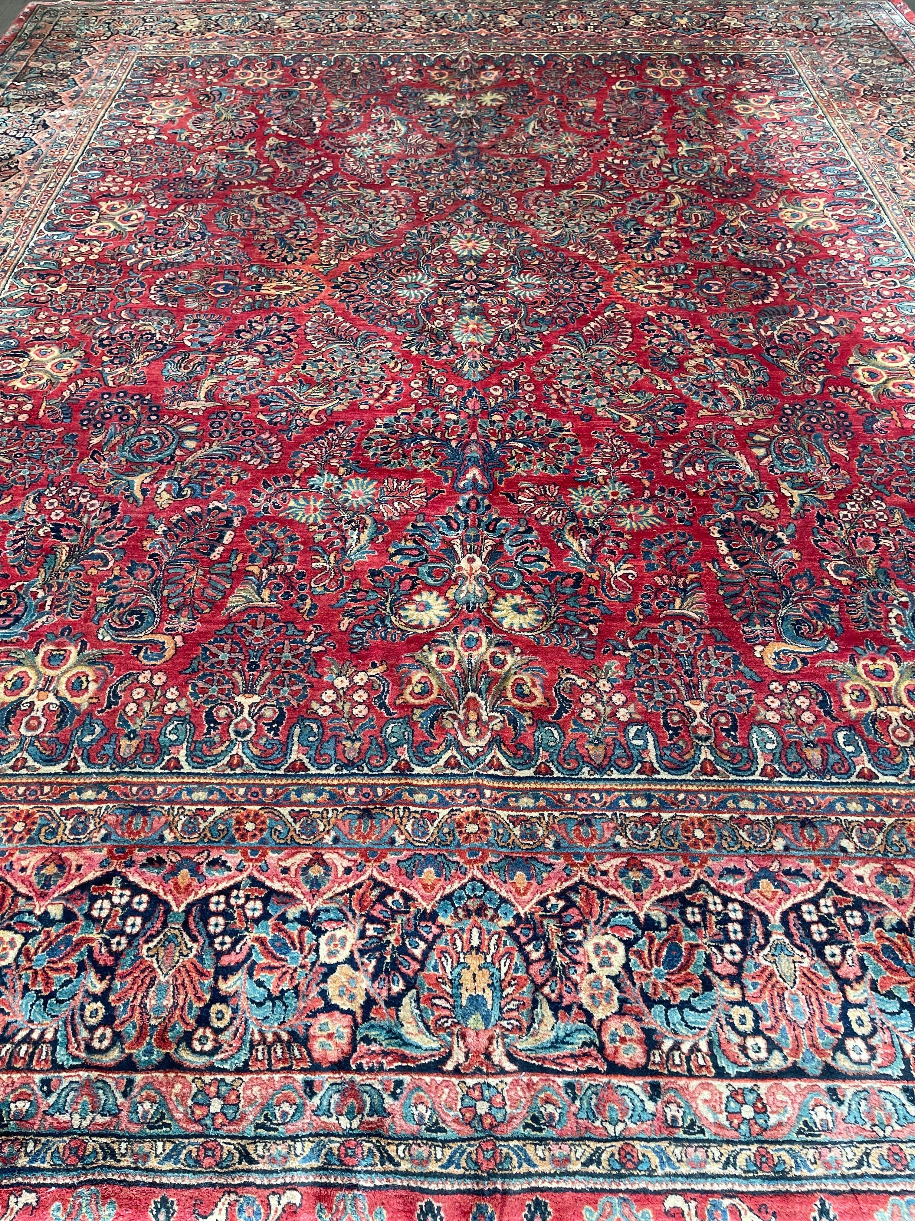 Absolutely flawless antique Persian Sarouk featuring a red/maroon field surrounded by a navy blue border.This classic rug is decorated with large flowers and a very small floral medallion. The rug is made with superb resilient and well pounded wool