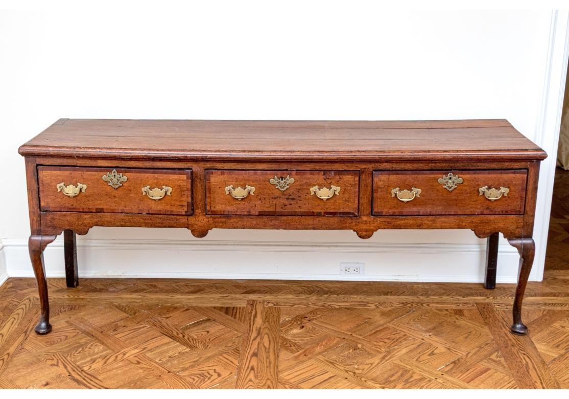A particularly fine antique Hunt Board likely 18th Century. The Board with  Queen Anne and Welsh influence in medium wood stain. The Board 
 features a long rectangular top with an ogee edge overhanging a case of three banded drawers all having