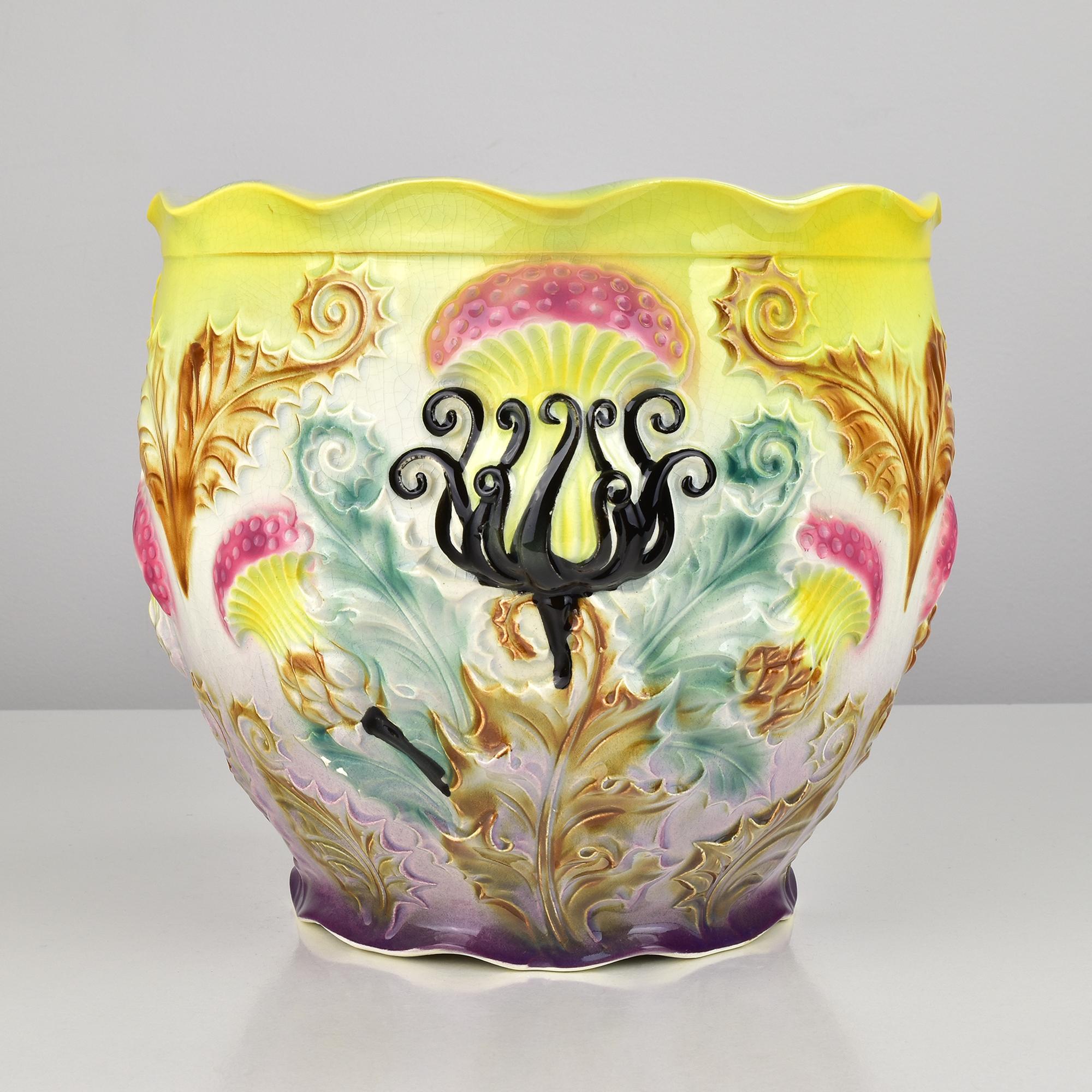 A highly decorative and vividly colored Art Nouveau Majolica jardinière or flowerpot, dating from circa 1900. This exuberant barbotine piece features an ornate relief design dominated by stylized thistles and curling leaves. The vibrant color