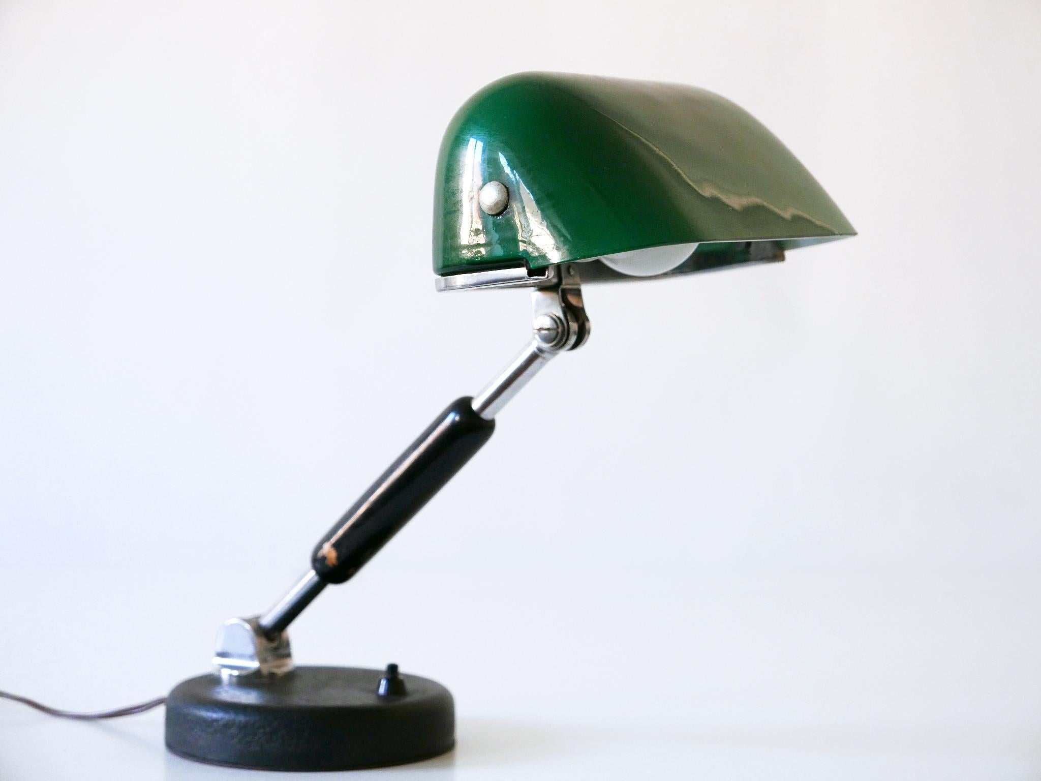 Rare and elegant Bauhaus / Modernist bankers table lamp or desk light. Adjustable arm and shade. Designed and manufactured, in 1930s, Germany. Interrupter on the base.

Executed in nickel-plated brass, thick green glass, black lacquered wood and
