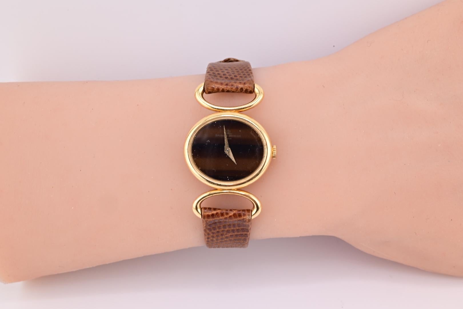 Cette exquise montre pour femmes Baume & Mercier est un ajout intemporel à toute collection. Fabriquée en or 18 carats, cette montre-bracelet présente un boîtier rond et un affichage analogique élégant. Le bracelet en cuir marron riche complète le