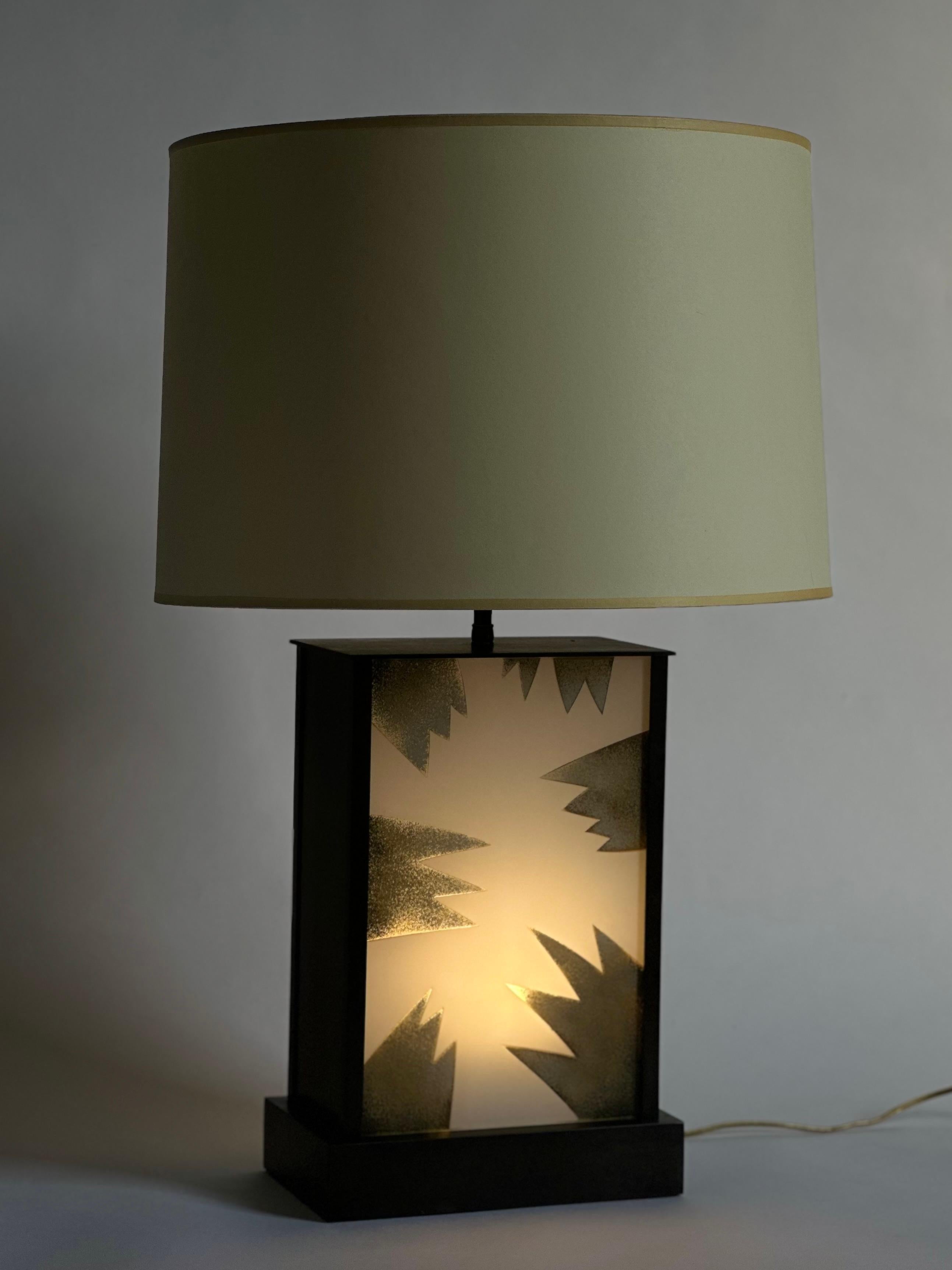 An unusual modern table lamp comprising a bronze or bronzed metal rectangular base that illuminates two reverse etched and painted glass panels (design motif is the same on both sides). The base can be lit independently from or along with the 2 main