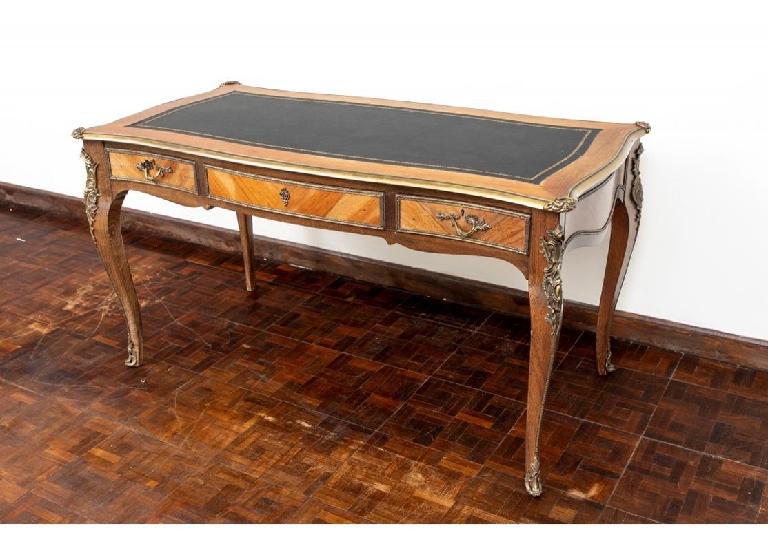 A very well-made French desk with lovely chosen and contrasting woods, serpentine form and bronze mounts on the corners, legs and feet with the top edges also bronze clad. The drawer fronts have bronze framing and traditional French pulls, and the