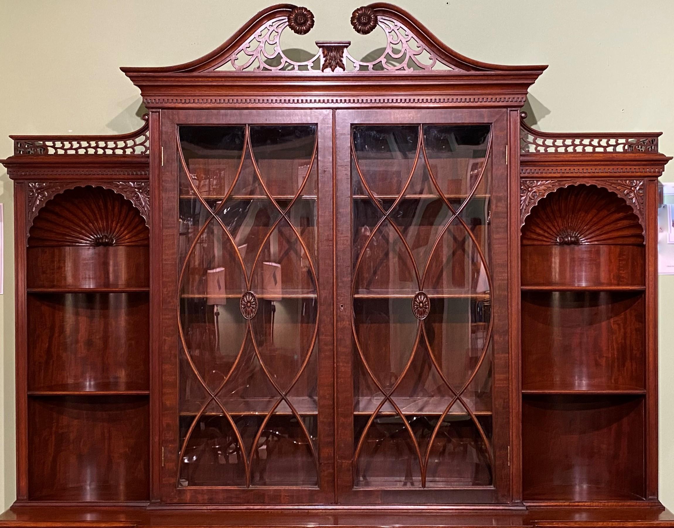An exceptional custom two part mahogany breakfront server cabinet or bookcase by Joseph Gerte of Boston, MA, its upper case featuring a crest with center swan’s neck broken arch pediment with carved rosettes and foliate fretwork, surmounting a
