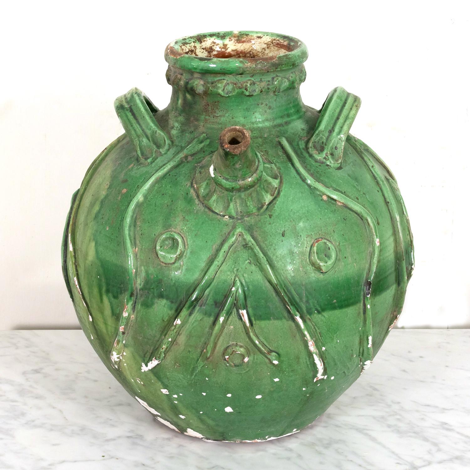 A large and exceptional early 19th century French terracotta walnut oil jug, probably from the Auvergne region, with a beautiful and vibrant green glaze, circa 1810s. Having a round shaped belly with three high arching looped handles and a pouring