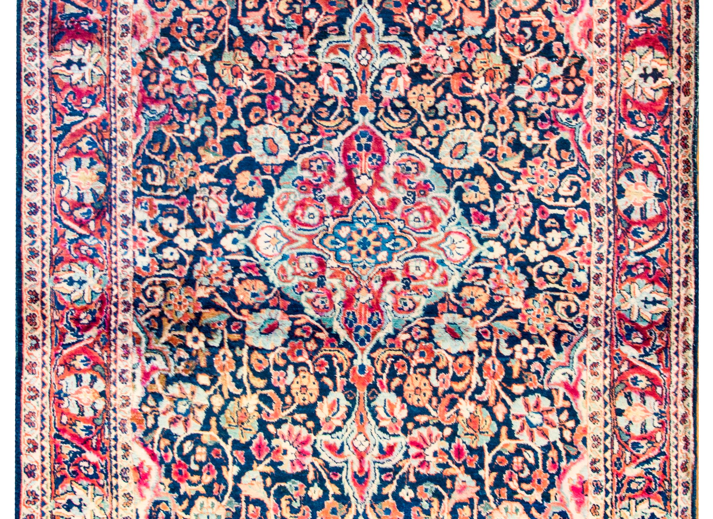 An exceptional early 20th century Persian Kashan rug with a densely woven field and medallion of myriad flowers, leaves, and vines, all woven in crimson, indigo, gold, pink, and cream colored vegetable dyed wool. The border is complex and as densely