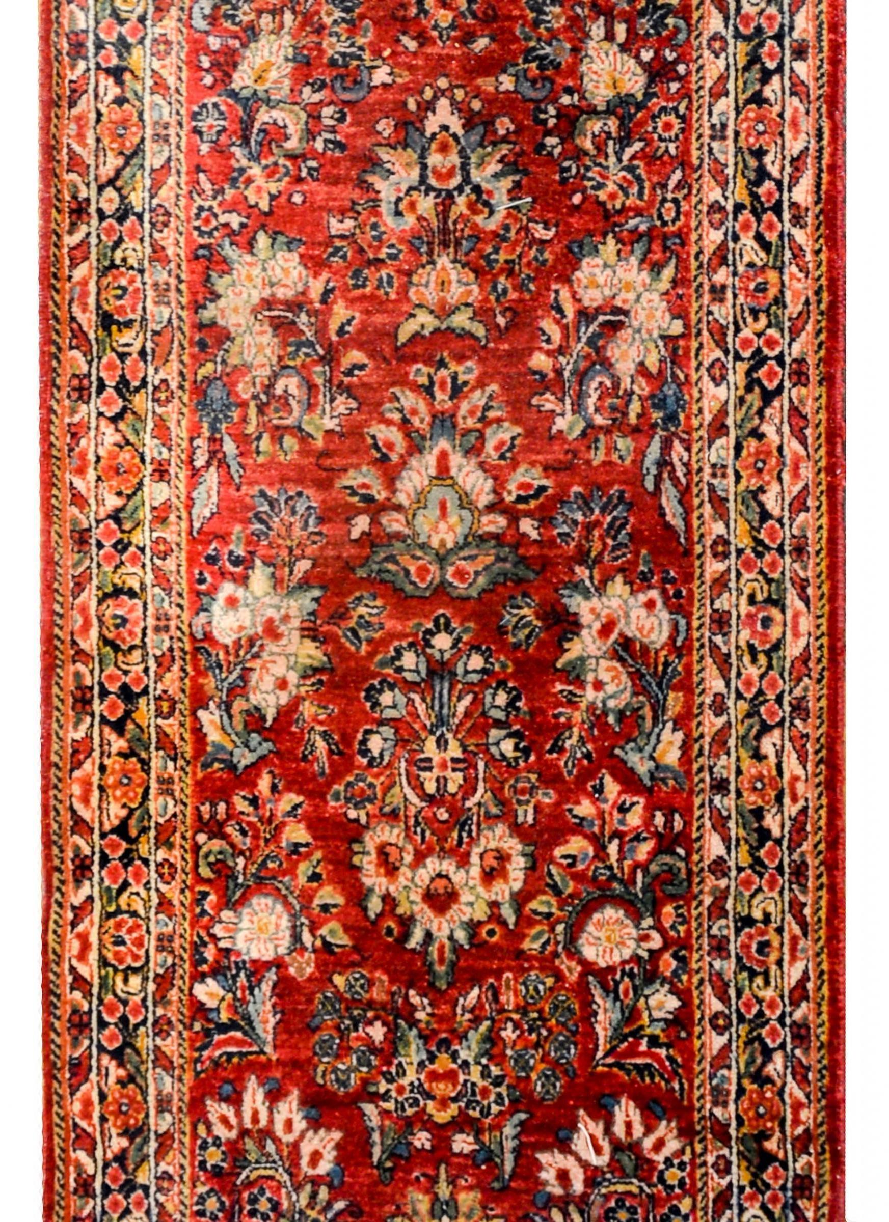 A beautiful early 20th century Persian Sarouk runner with a fantastic mirrored floral and vine pattern, expertly rendered, in light and dark indigo, salmon, gold, on a bold crimson background. The border is wide, with multiple floral and stylized