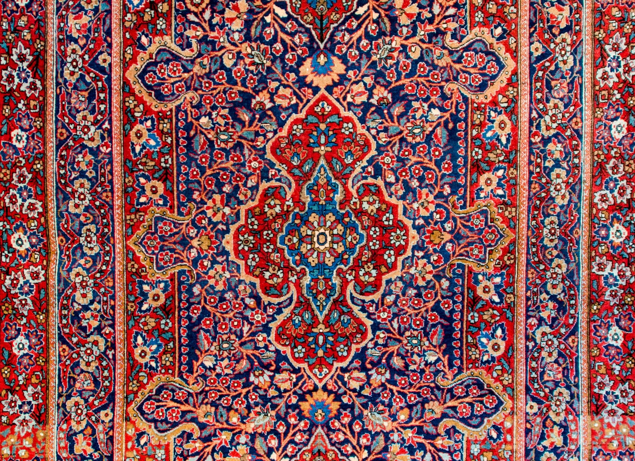 An exceptional early 20th century Persian Kashan rug with a densely woven field and medallion of myriad flowers, leaves, and vines, all woven in crimson, indigo, gold, pink, and cream colored vegetable dyed wool. The border is complex and as densely