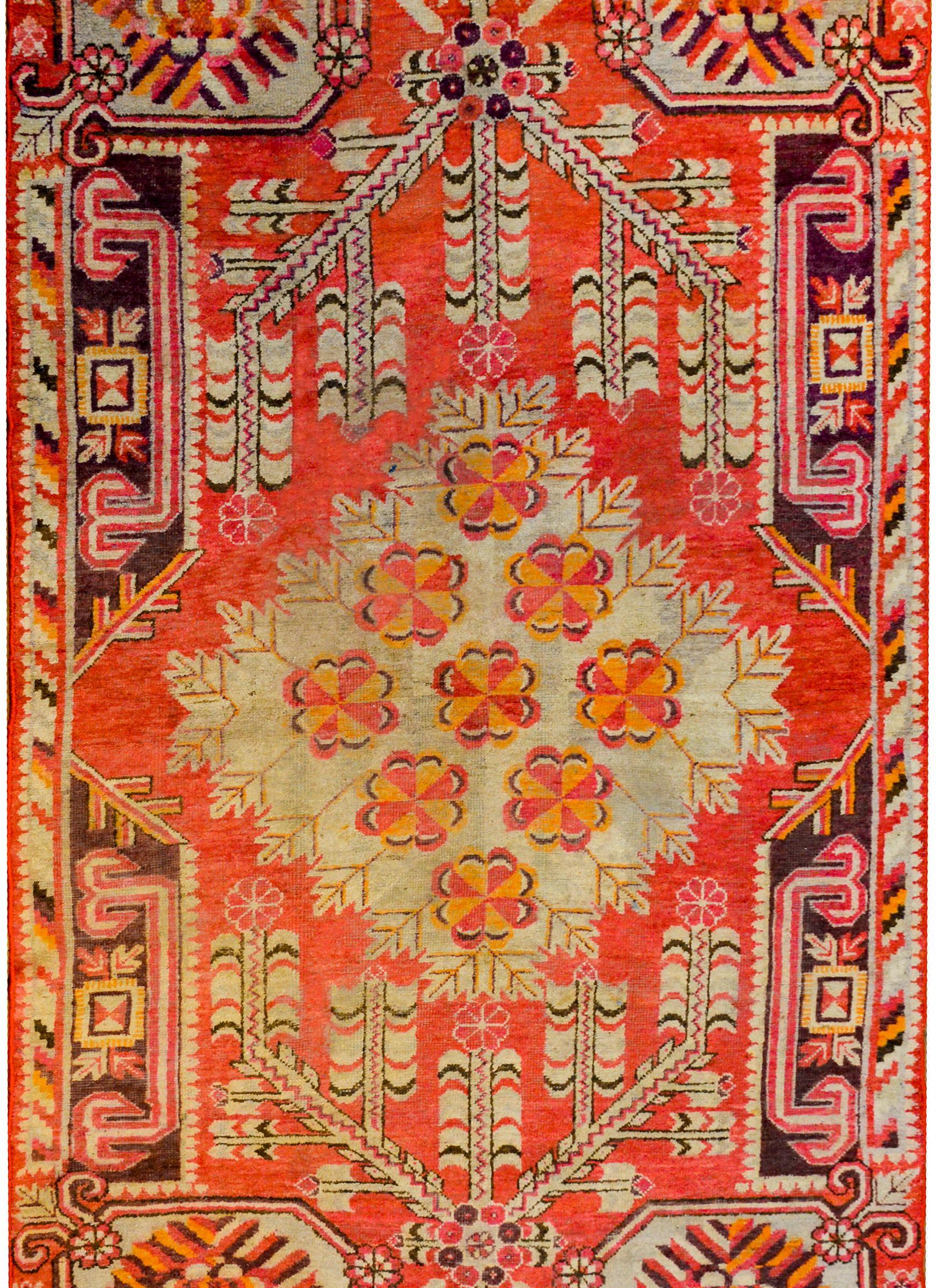 An exceptional early 20th century Central Asian Khotan rug with a fantastic central diamond medallion with multiple pink and orange flowers amidst a field of branches with leaves on a rich coral colored background. The border is wonderful with a