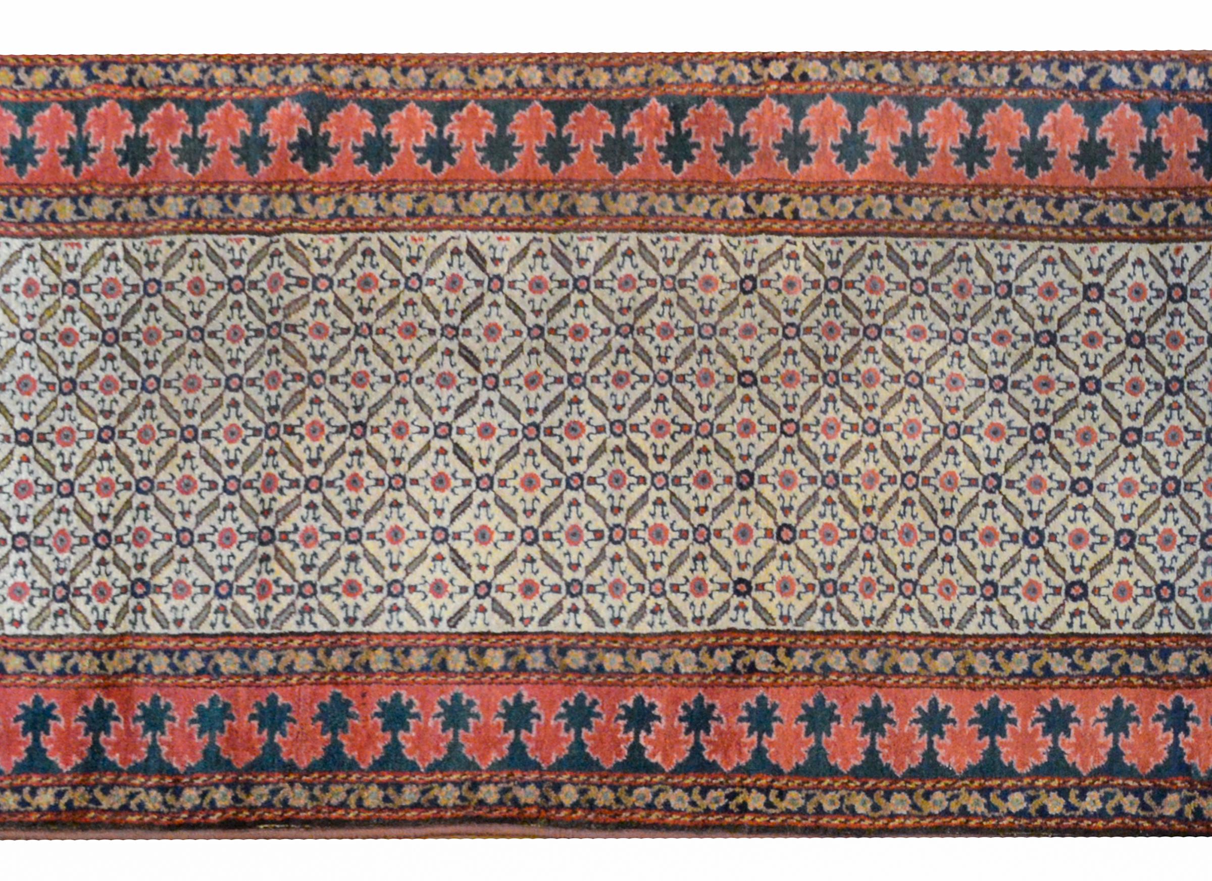 An exceptional early 20th century Malayer runner with an all-over trellis and floral pattern woven in crimson, indigo, and pale yellow, surrounded by a wide border of alternating crimson and indigo flowers flanked by a pair of petite floral