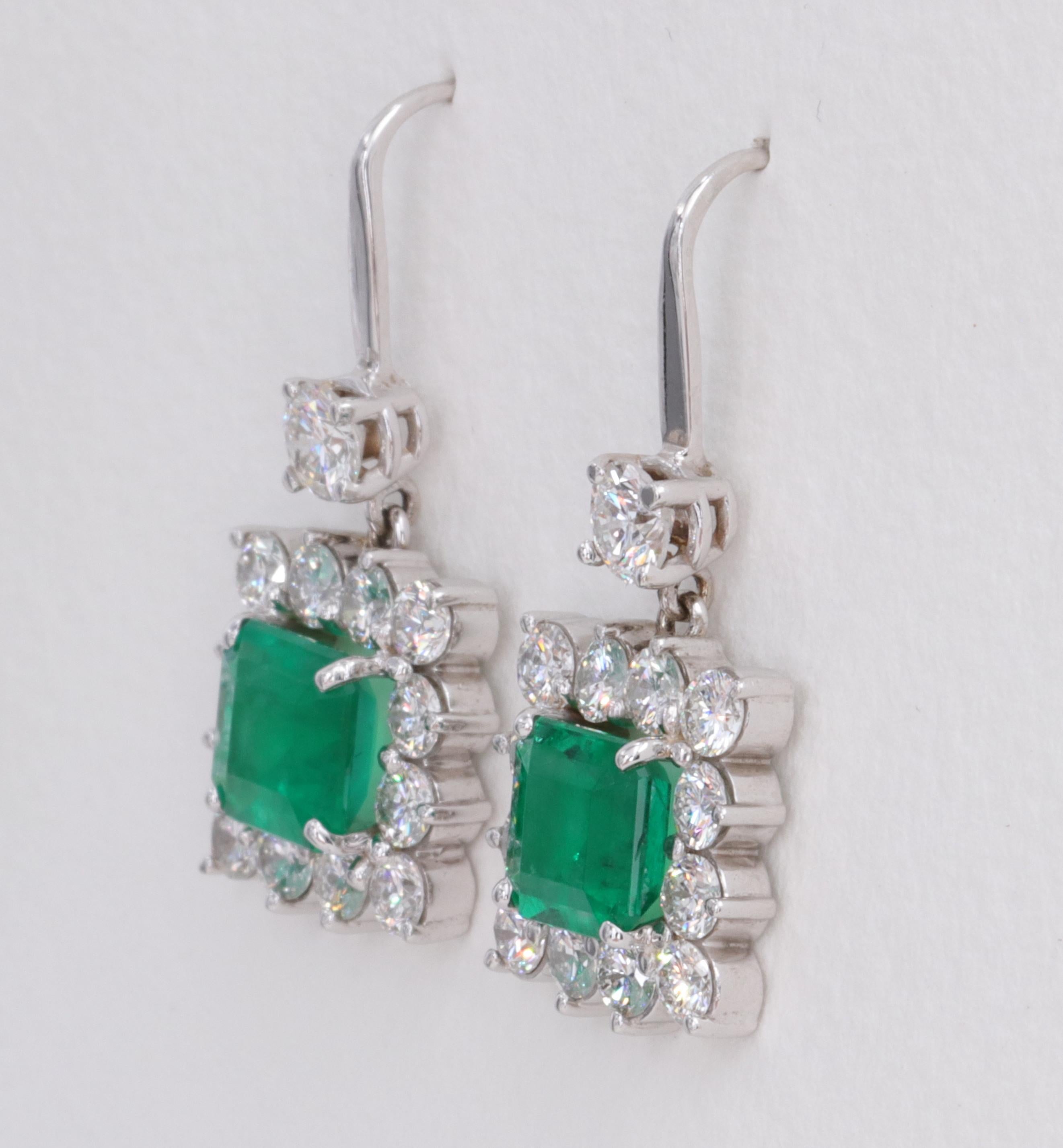 Emerald Cut Exceptional Emerald and Diamond Halo Dangle Earrings Set in 18 Karat White Gold For Sale