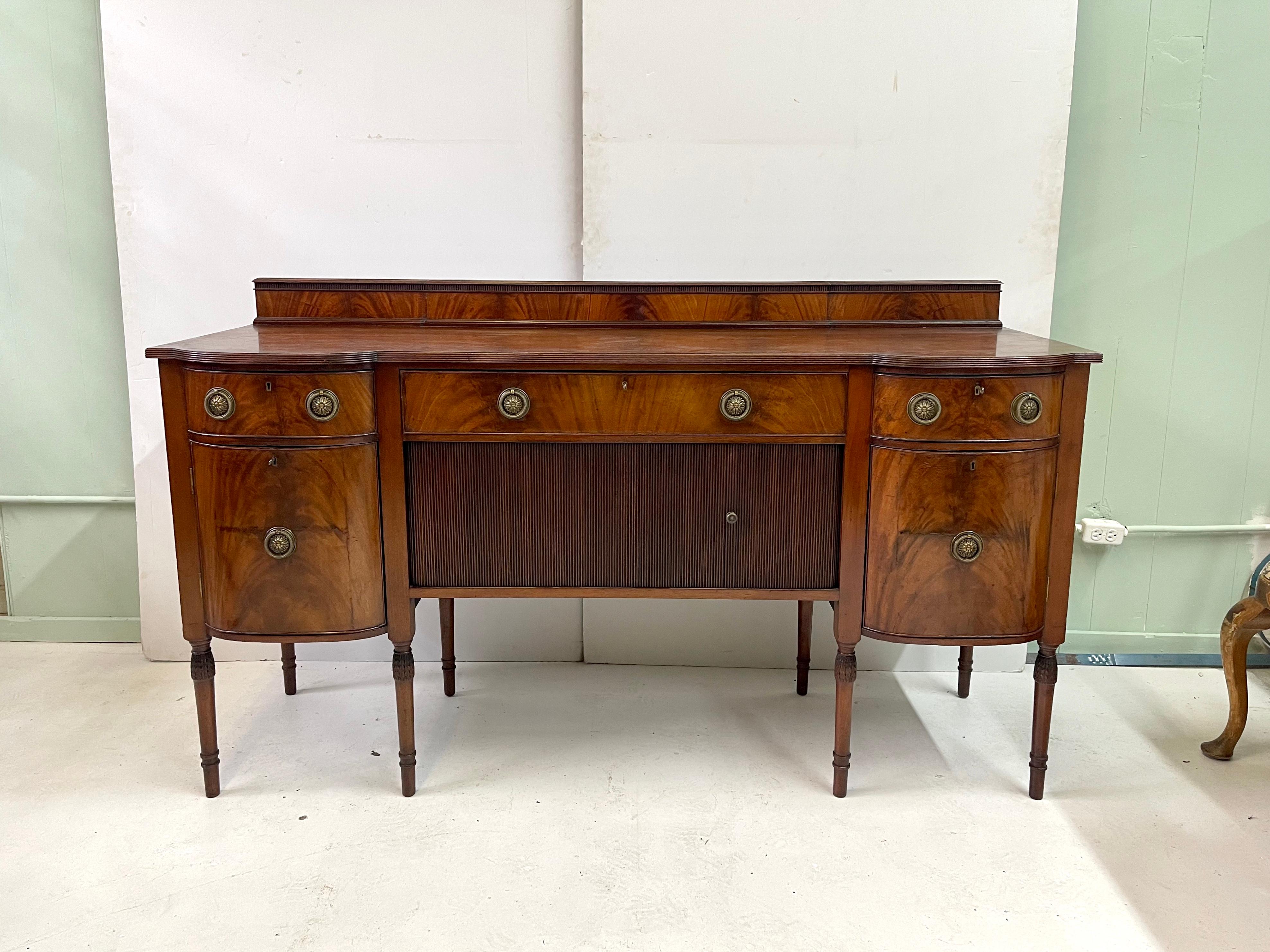 Exceptional quality 19th century English Georgian sideboard of flame mahogany. The one board top is beautifully shaped with an intricate reeded edge detail and a decorative backsplash. In the sideboard's frieze is a wide center drawer flanked by a