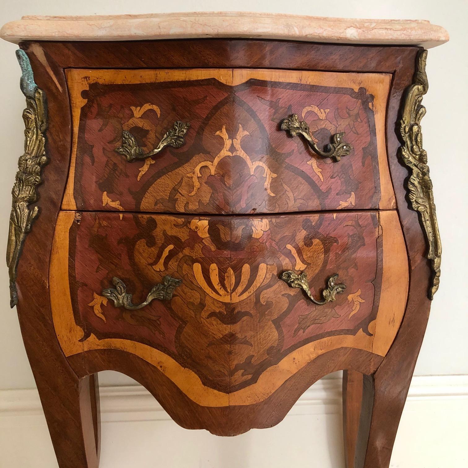 An exceptional Louis XV style mahogany nightstand or side end table having
 gorgeous mahogany wood grain with inlaid marquetry and a pink beveled marble top. The nightstand offer two drawers, and the cases rest on tall cabriole legs with mounted