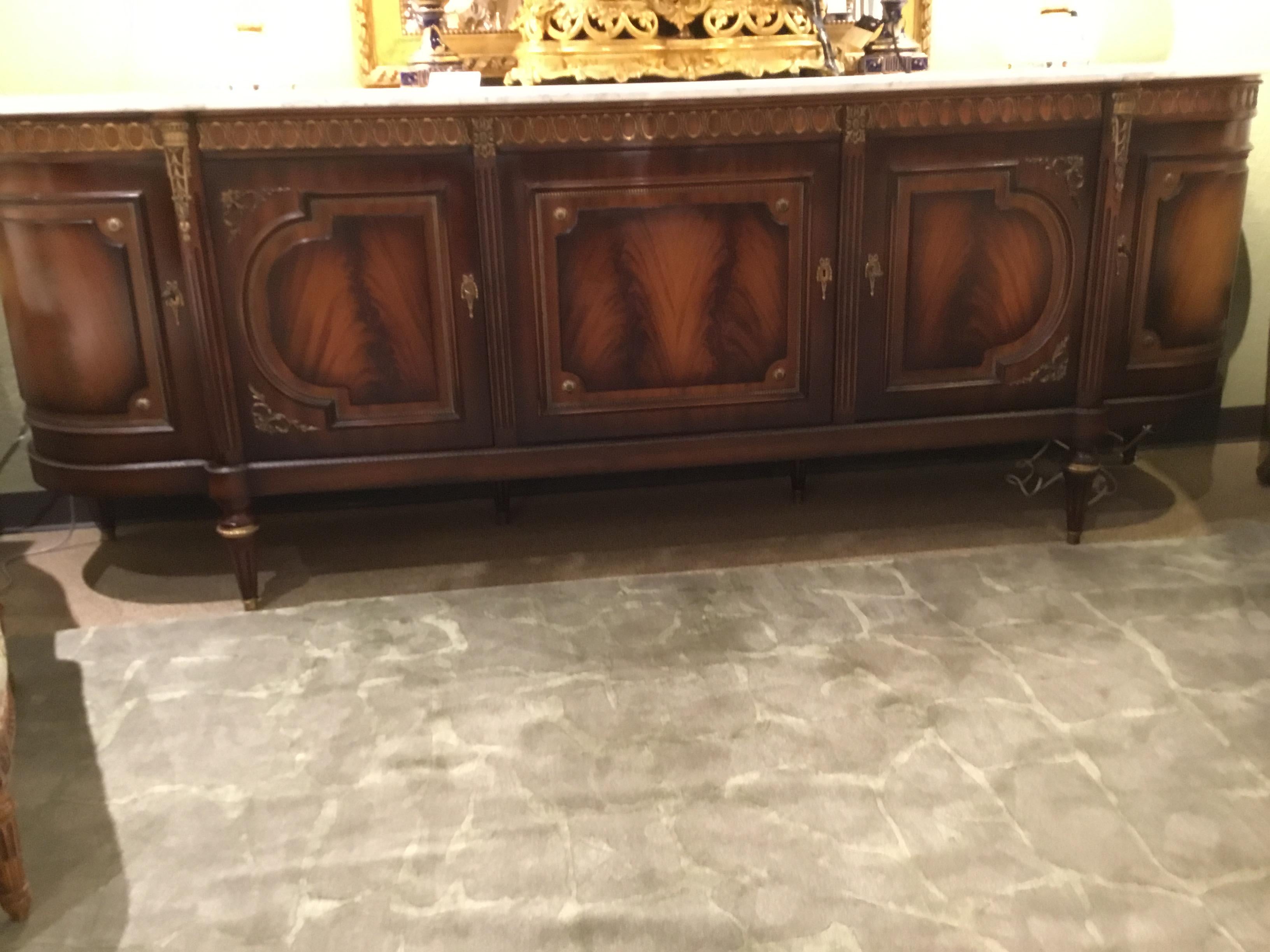 Mahogany sideboard in Louis XVI style, signed JP Ehalt, having a white marble top above curved 
Case with gilt metal accents throughout, far left opens to a bar cabinet with mirrored back with
Two glass shelves, beside that cabinet door opens to