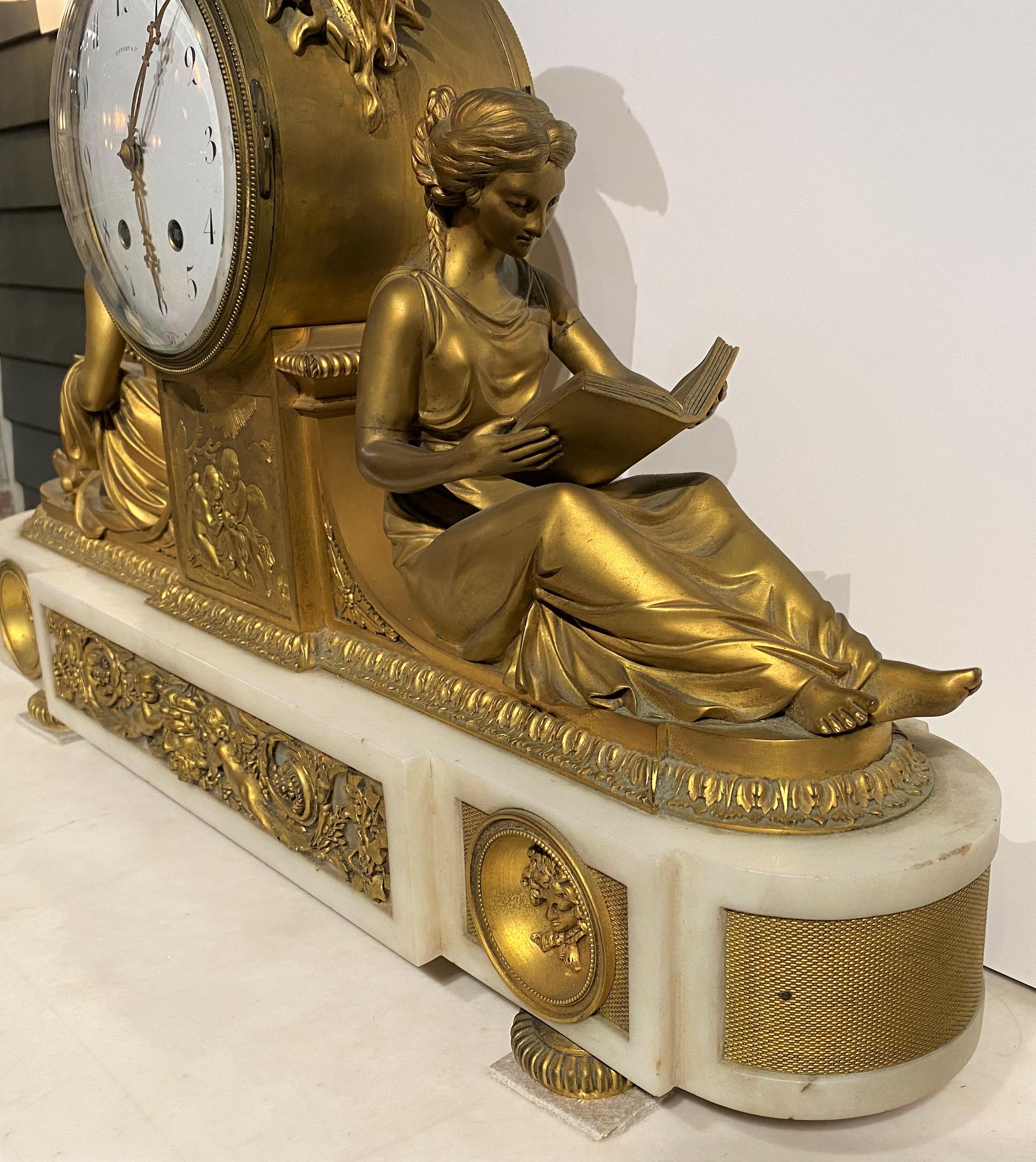 An exceptional French gilt bronze mantel clock marketed by Tiffany & Co, with classical cast gilt figures of a boy and girl reading on each side of the clock, a central raised panel with cherubs below the enameled dial, applied ormolu with faces and