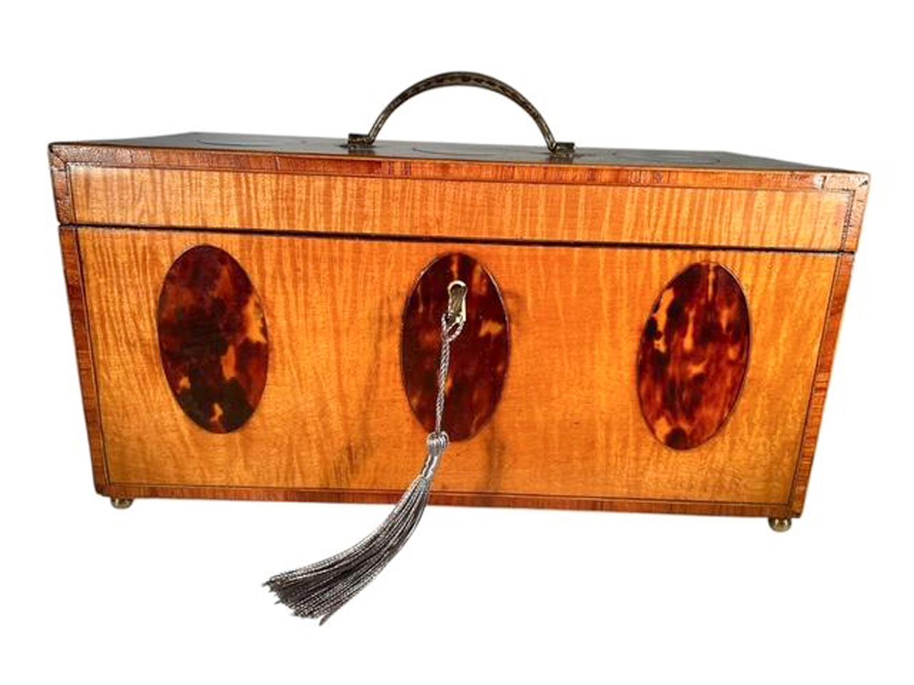 A fine tea chest or tea caddy in satinwood with crossbanded edges on the lid and all four sides, the lid, front and sides inlaid with ovals of tortoiseshell. The lid, centered with an engraved bail handle opens to an interior with two removeable