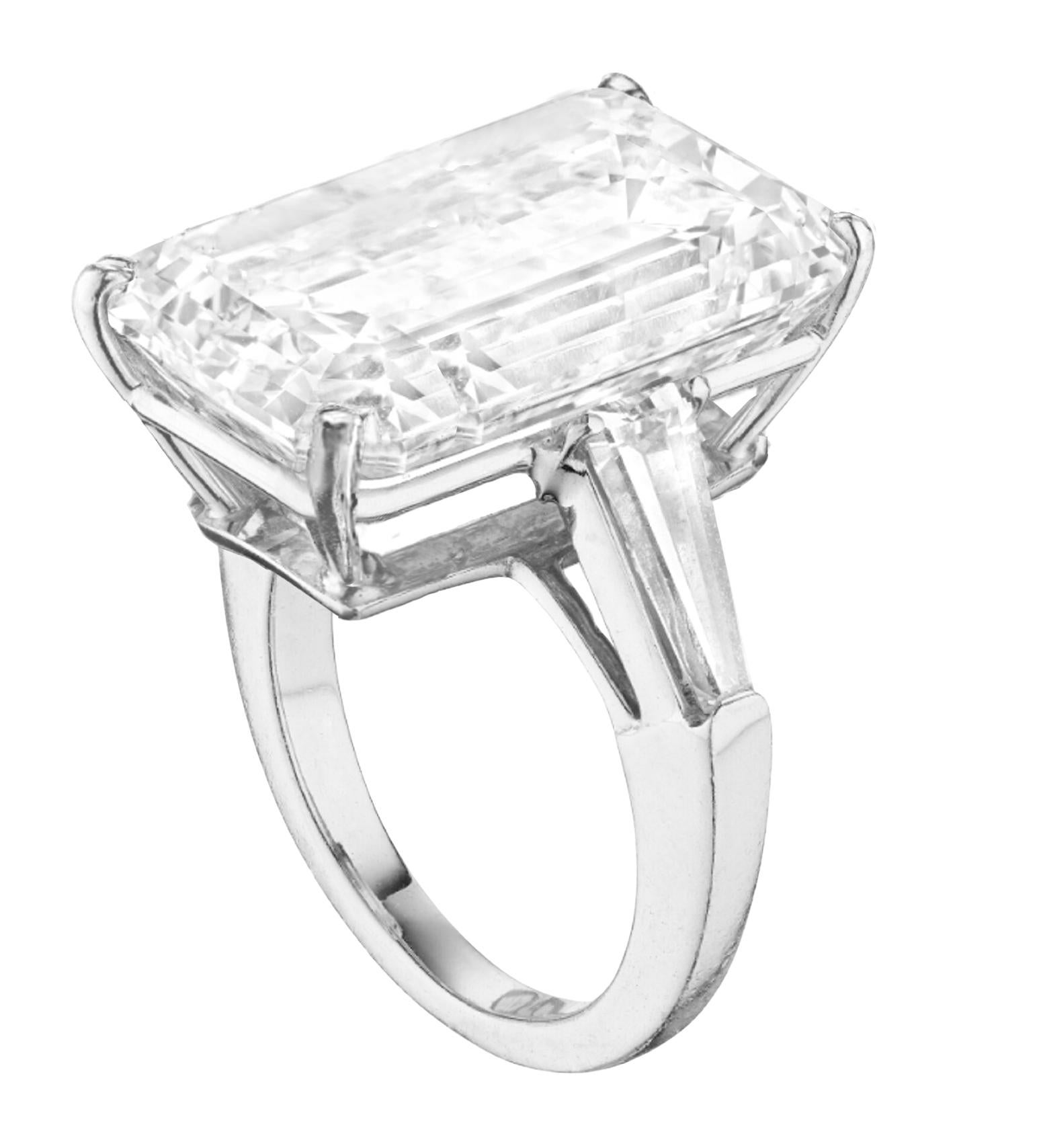 Dieser außergewöhnliche Ring mit drei Steinen präsentiert einen 8.26 Karat schweren Diamanten im Smaragdschliff von unvergleichlicher Brillanz. Das in luxuriösem Platin gefasste Design wird durch spitz zulaufende Baguette-Diamanten auf jeder Seite