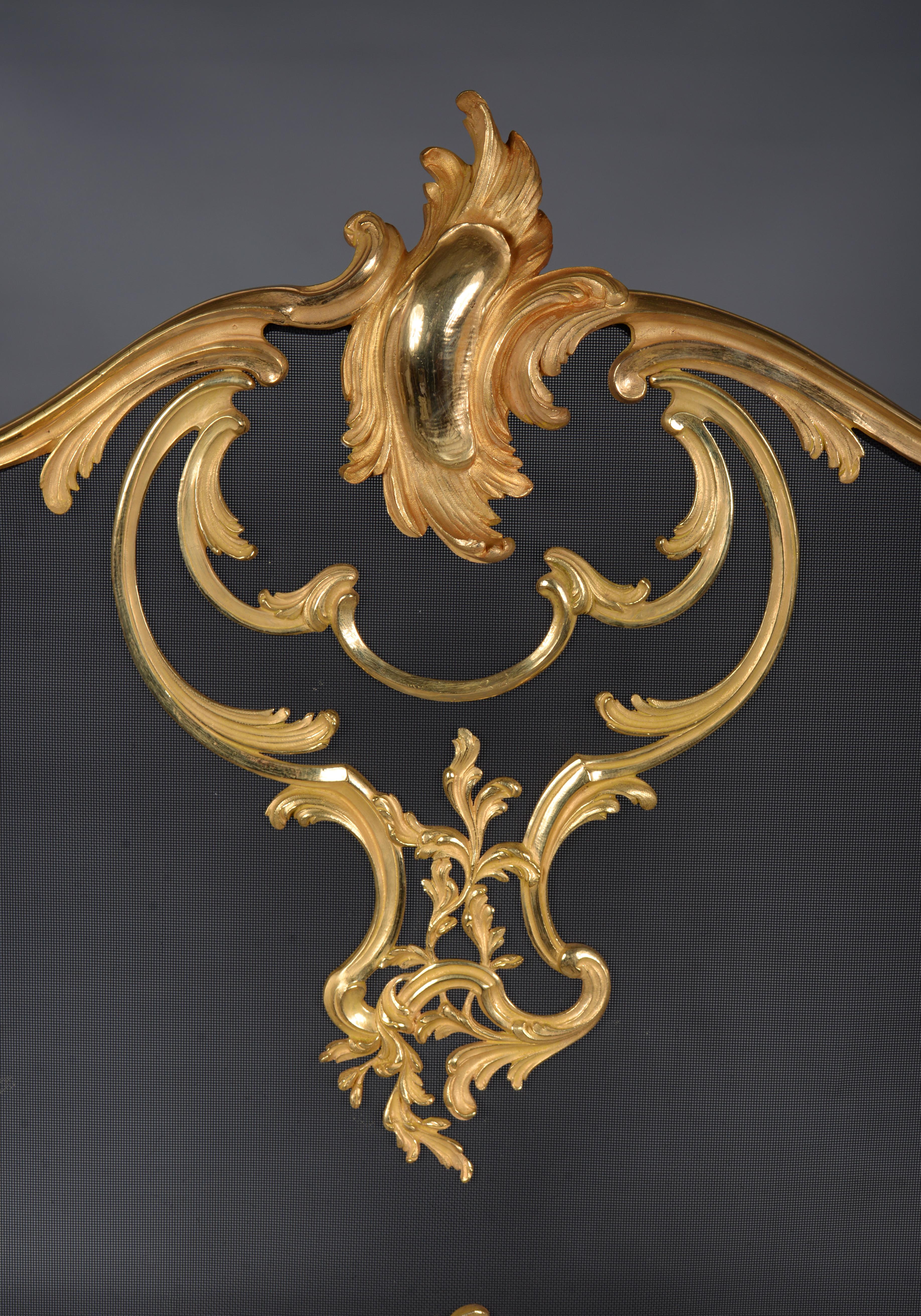Ce bel écran de cheminée en bronze doré est une réédition d'un modèle présenté à l'Exposition universelle de 1900 par le grand spécialiste des accessoires de cheminée, Bouhon Frères. Reprenant les lignes courbes du style Louis XV, notre pare-feu est