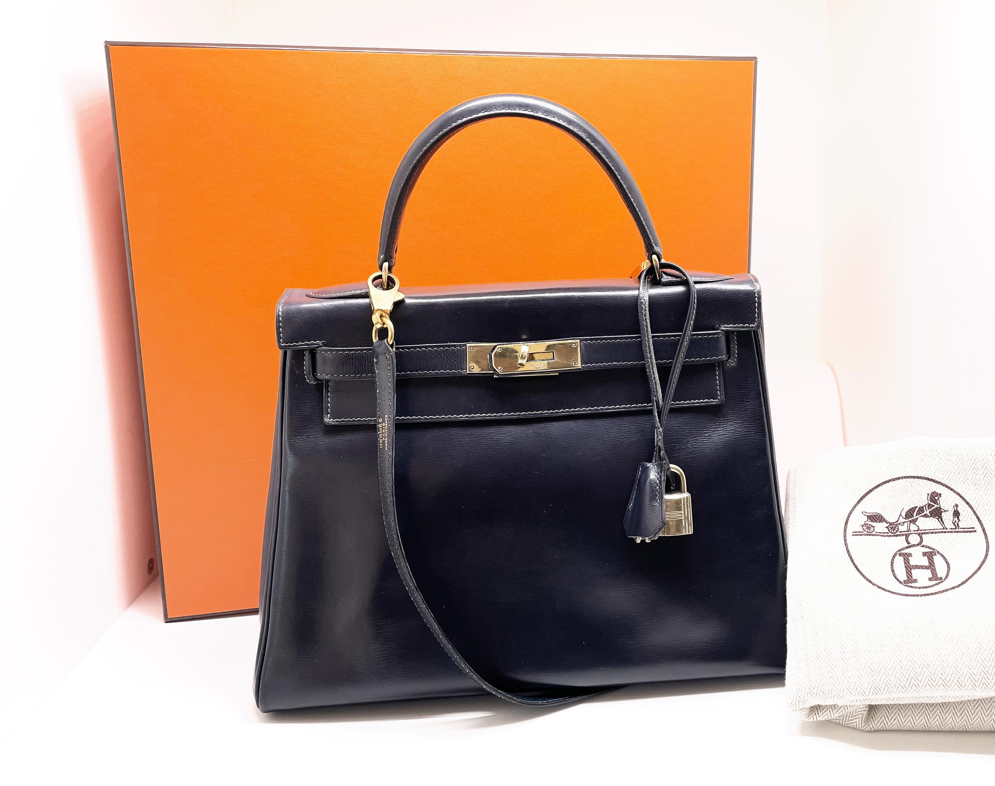 Exceptional​ ​Hermès​ ​Kelly​ ​bag​ ​28​ ​returned​ ​in​ ​navy​ ​box​ ​leather,​ ​gold-plated​ ​metal​ ​trimming,​ ​shoulder strap​ removable​ ​in​ ​marine​ ​box​ ​leather,​ ​handle​ ​in​ ​marine​ ​box​ ​leather​ ​allowing​ ​carrying​ ​in the hand​