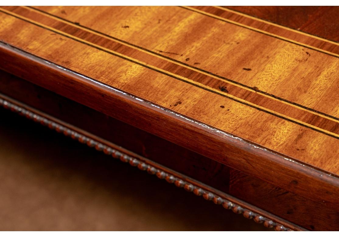 Produite aux Philippines, cette  La très belle table de salle à manger de Whiting est composée de solides et de placages d'acajou. Les tons riches et chauds du bois d'acajou, combinés à la marqueterie en bande sur le dessus, offrent une grande