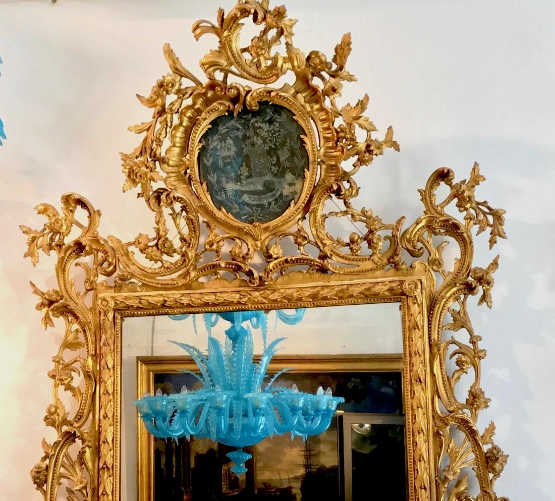 A very Fine Italian carved and giltwood mirror,
 Tuscany mid-18th century.
 Cresting above a cartouche shaped engraved mirror depicting an Architectural scene, above a rectangular plate within moulded frame carved with C-scrolls flowers and