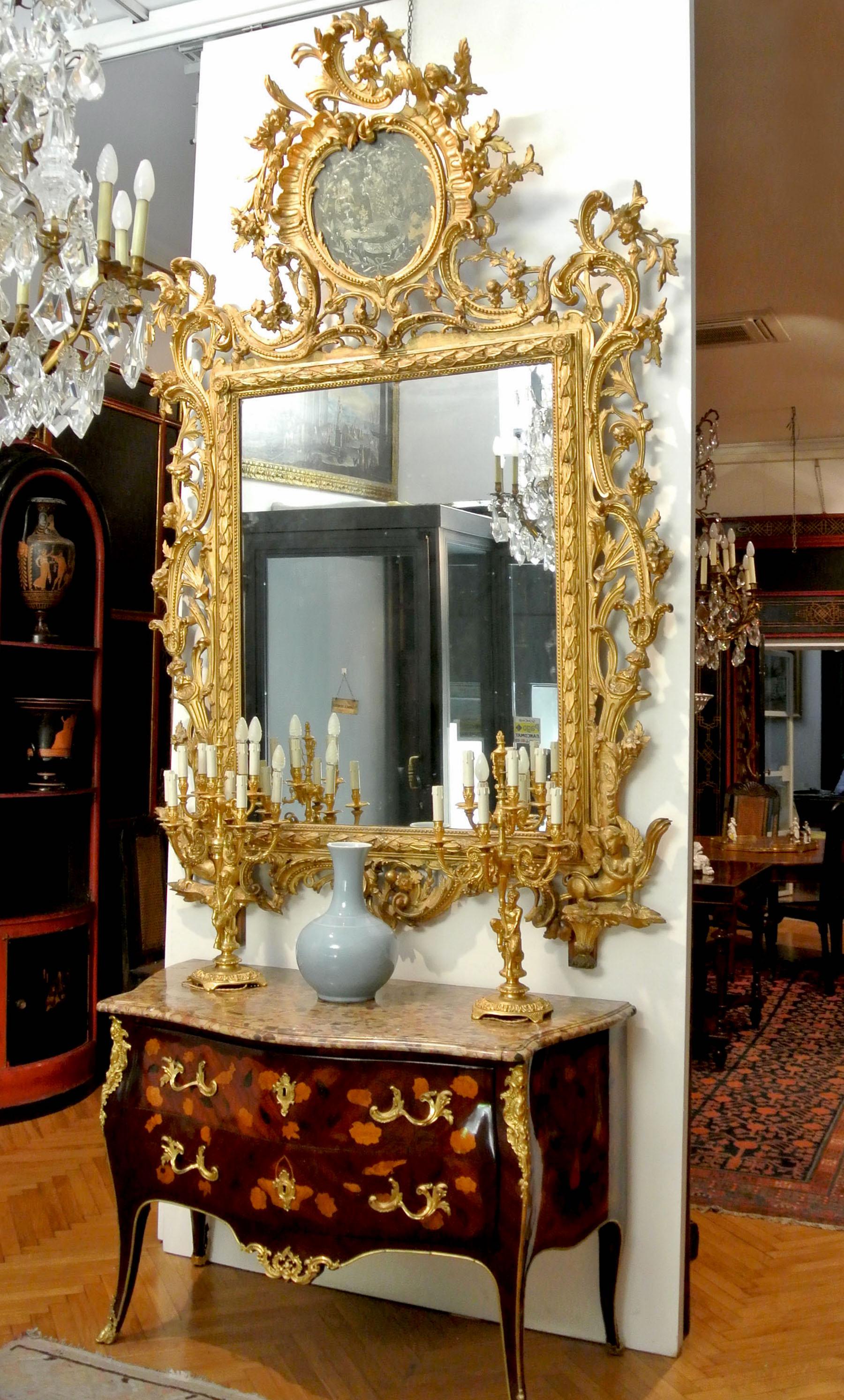 Très beau miroir italien en bois sculpté et doré,
 Toscane, milieu du XVIIIe siècle.
 Cresting above a cartouche shaped engraved mirror depicted an Architectural scene, above a rectangular plate within moulded frame carved with C-scrolls flowers