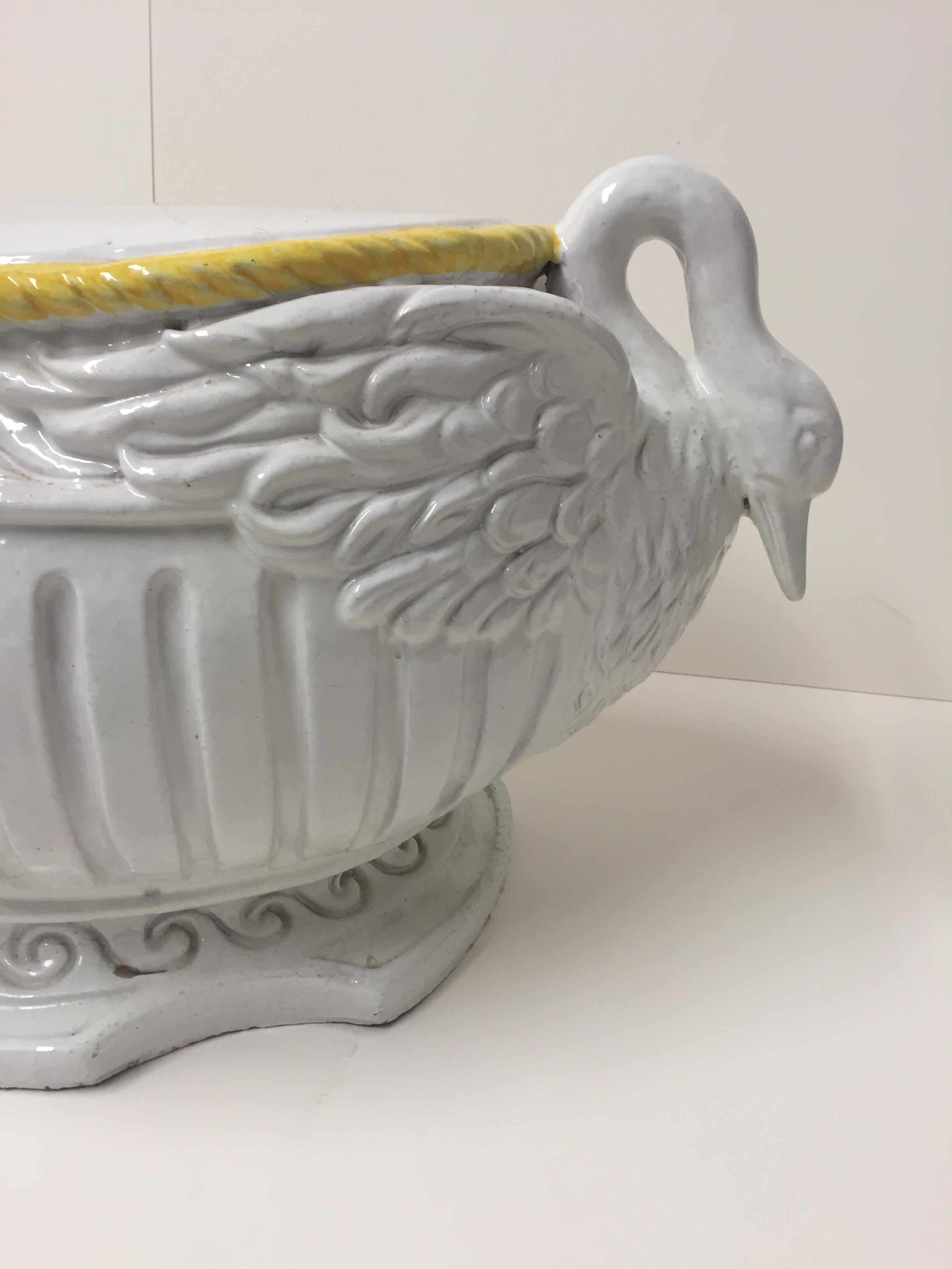 A rare form ceramic garden seat in white and yellow having a flat oval top and romantic decorative base with two swan heads adorning each side.