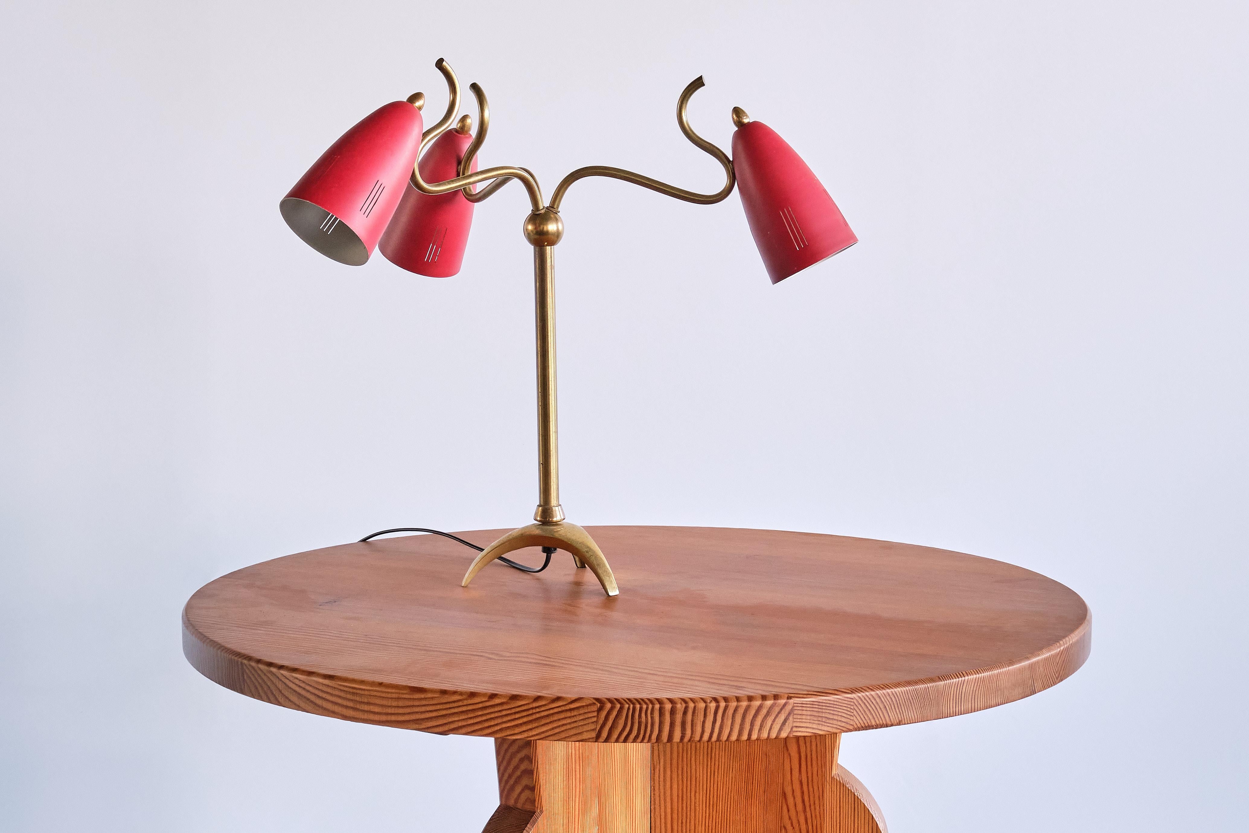 This exceptional three arm table lamp was produced in Italy in the early 1950s. The elegant design consists of a brass frame and three red shades.
The brass frame with a central, slightly raised tripod base and tubular central stem ending in a