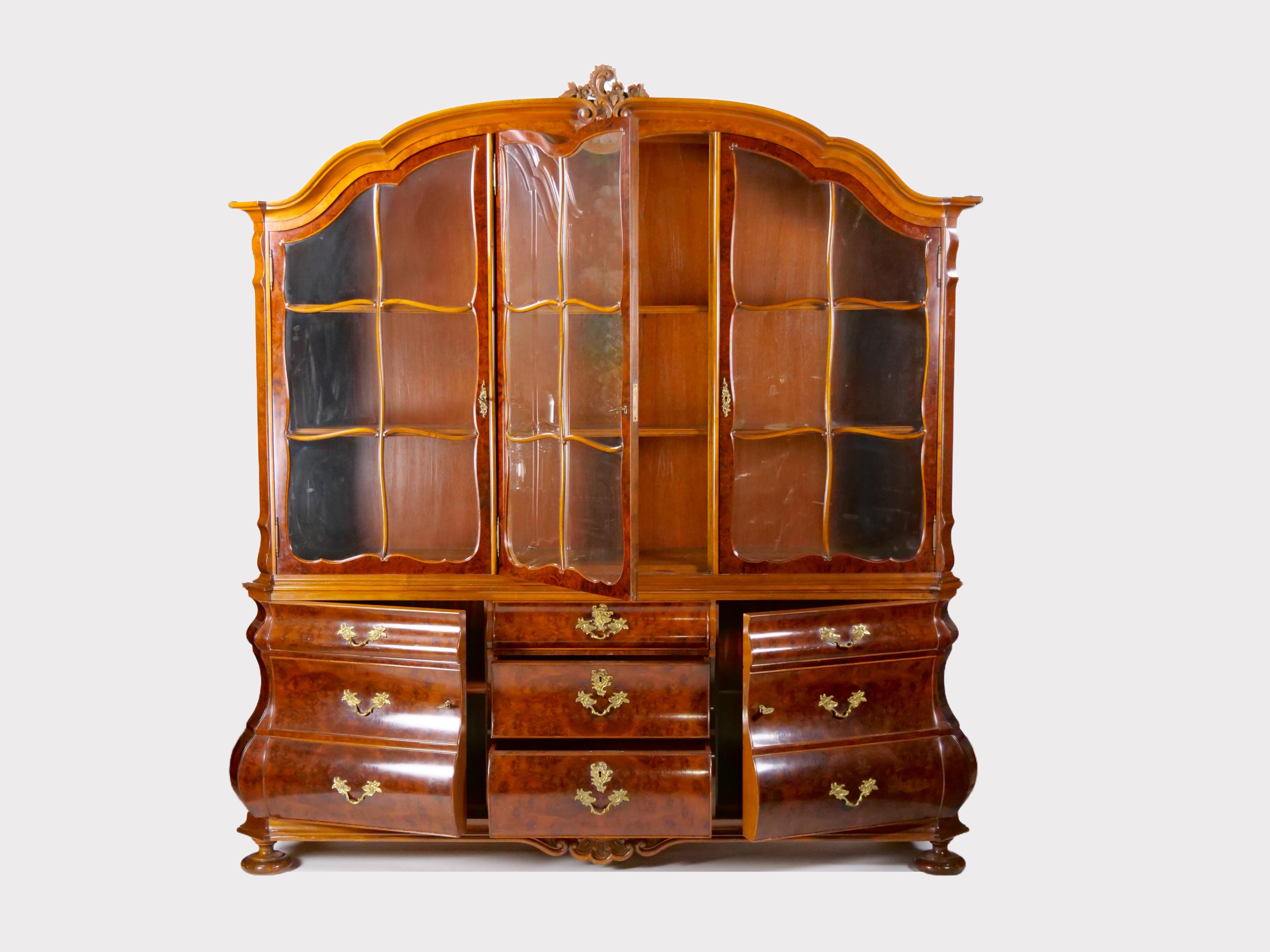 
Discover a truly exceptional and generously sized two part vitrine / display cabinet, expertly crafted in the opulent Dutch Baroque style. Its beauty lies in the exquisite walnut veneer that graces its surface, while finely carved accents adorn the