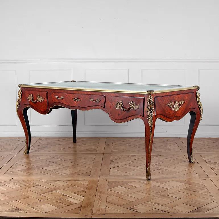 Questo eccezionale bureau plat in palissandro in stile Luigi XV presenta un piano in pelle lavorato a mano ed è ornato da elaborate decorazioni in ormolu (bronzo dorato). Le montature in ormolu, finemente fuse e dorate, includono abbellimenti