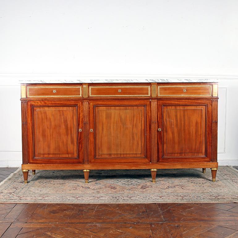 This early 20th century French Louis XVI style buffet is testament to the high quality workmanship and style Parisienne ateliers are known for. Handcrafted of mahogany and having a white molded Carrara marble top with a beveled edge over three
