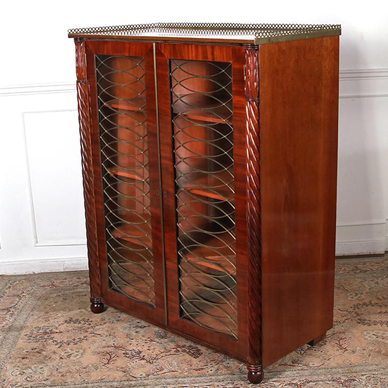 Early 19th century, Regency bookcase constructed of solid mahogany, featuring original glazed doors with striking solid brass grill work and the top is finished with a pierced brass gallery. Inside, the back curves elegantly at each side and the