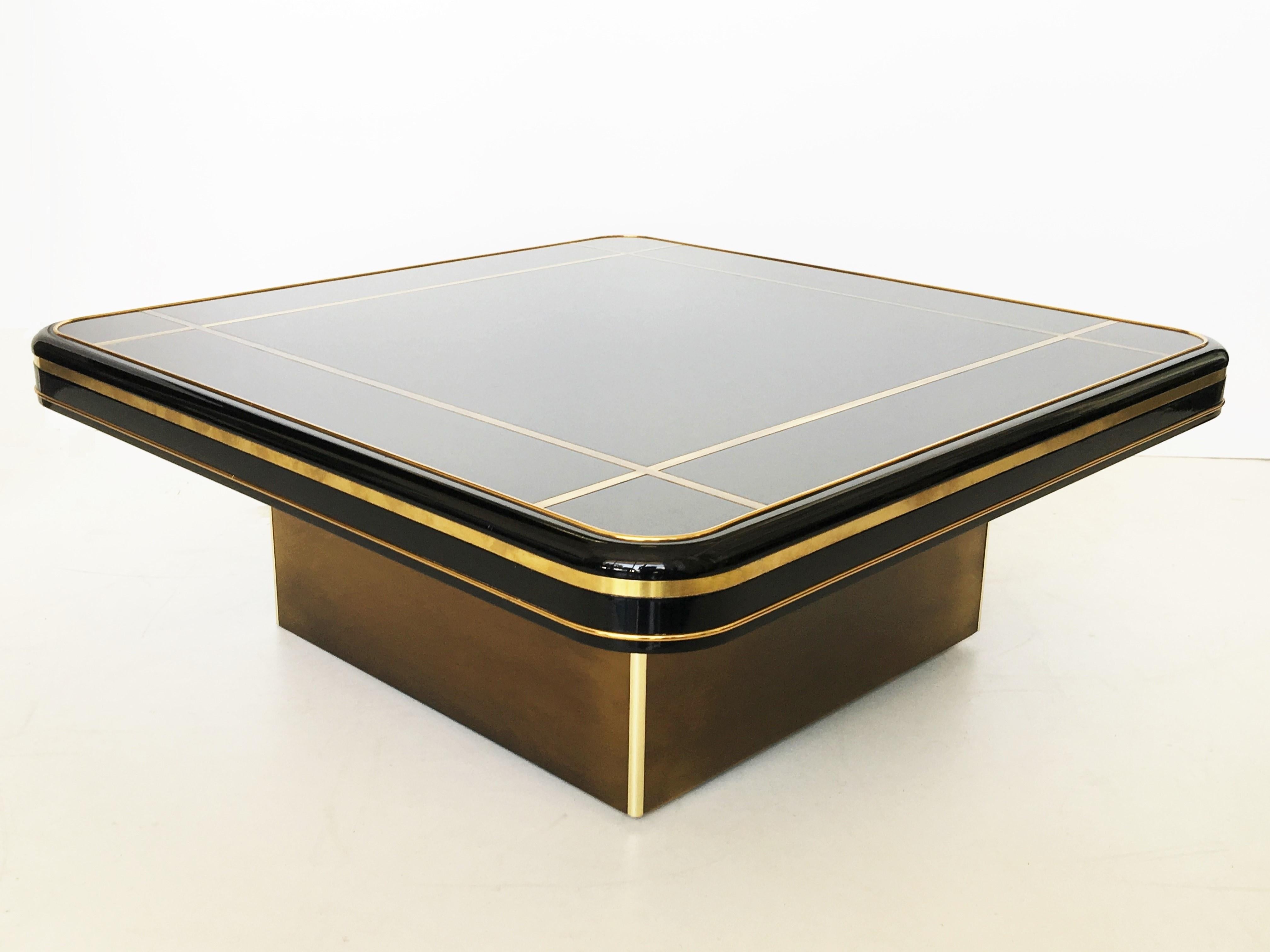 Mastercraft coffee table featuring a brass platform base supports a square top with inset dark brown surface and decorative brass banding, original finish.