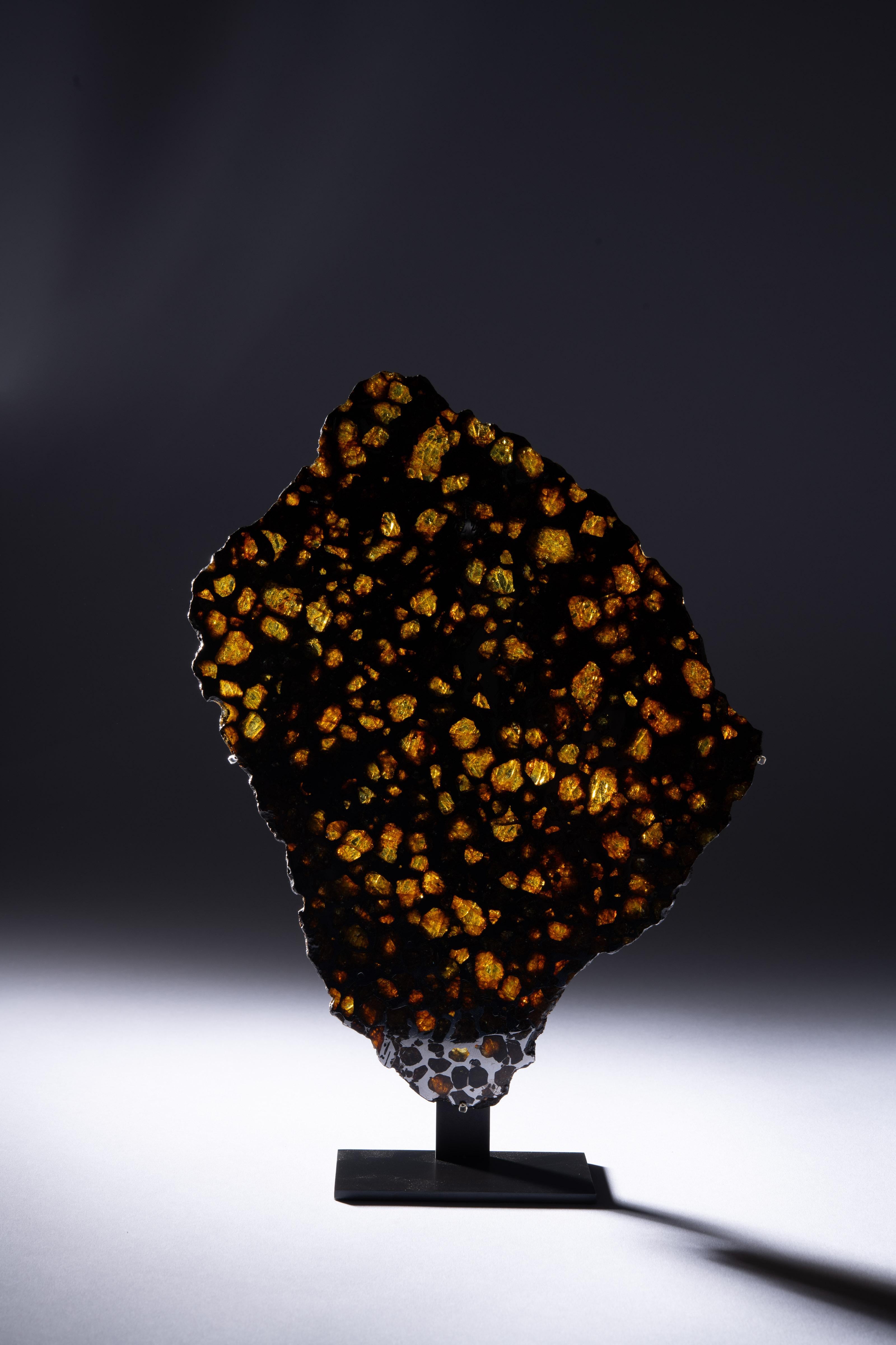 A complete cross section of one of the most beautiful meteorites known, displaying shimmering, translucent olivine and peridot gems, embedded in an iron-nickel metallic matrix.

The magnificent honeycomb pattern shown on the present specimen is