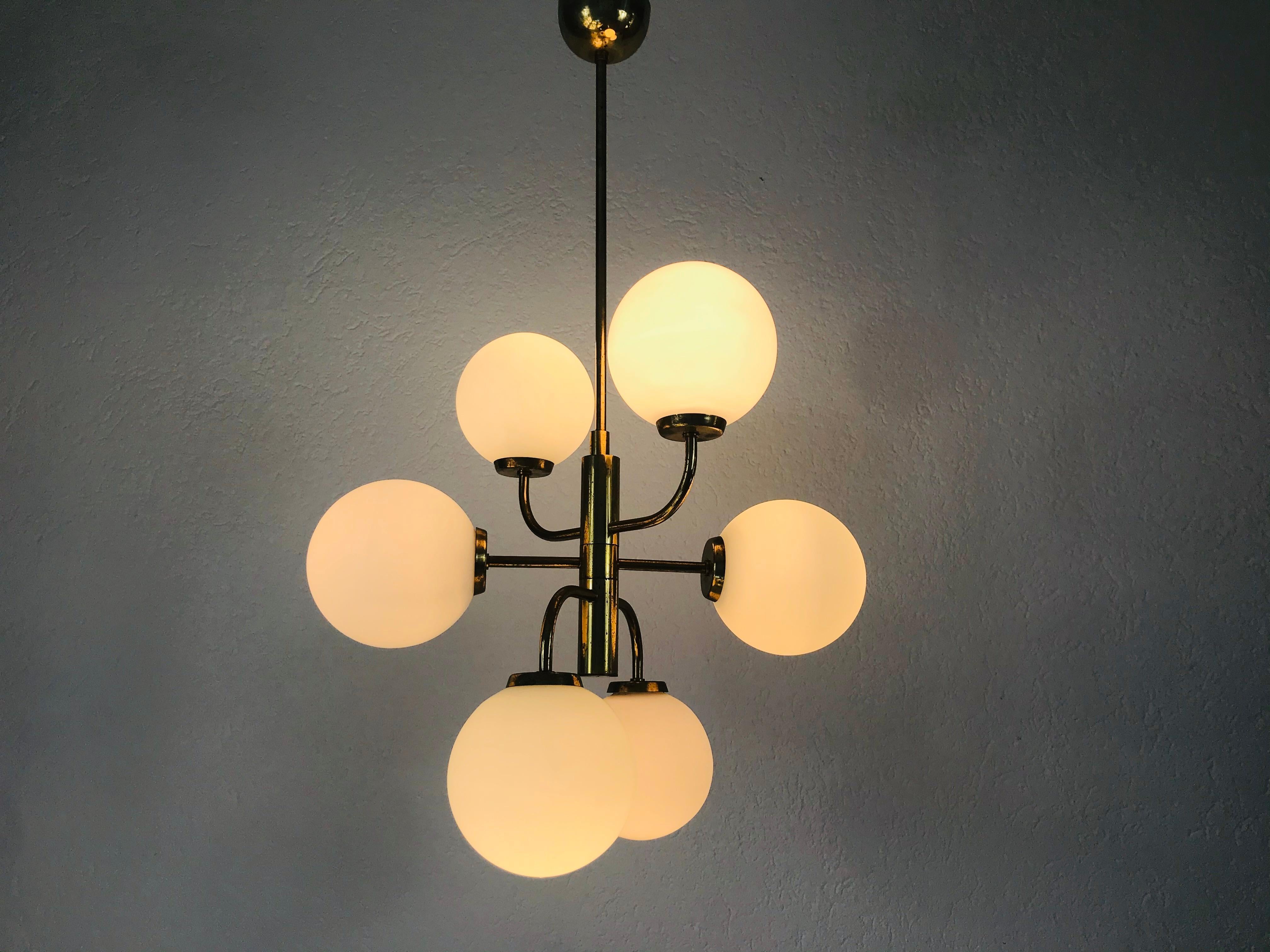 Un lustre Kaiser du milieu du siècle, fabriqué en Allemagne dans les années 1960. Il est fascinant avec son design de l'ère spatiale et ses six boules en verre opalin. Le corps circulaire de la lampe est en laiton poli, y compris les bras. 

Bon